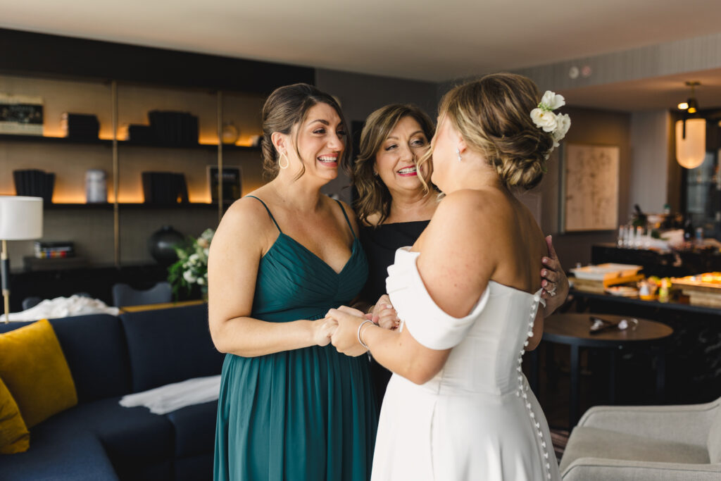 Mother of the bride and the bride's sister smiling emotionally at the bride.