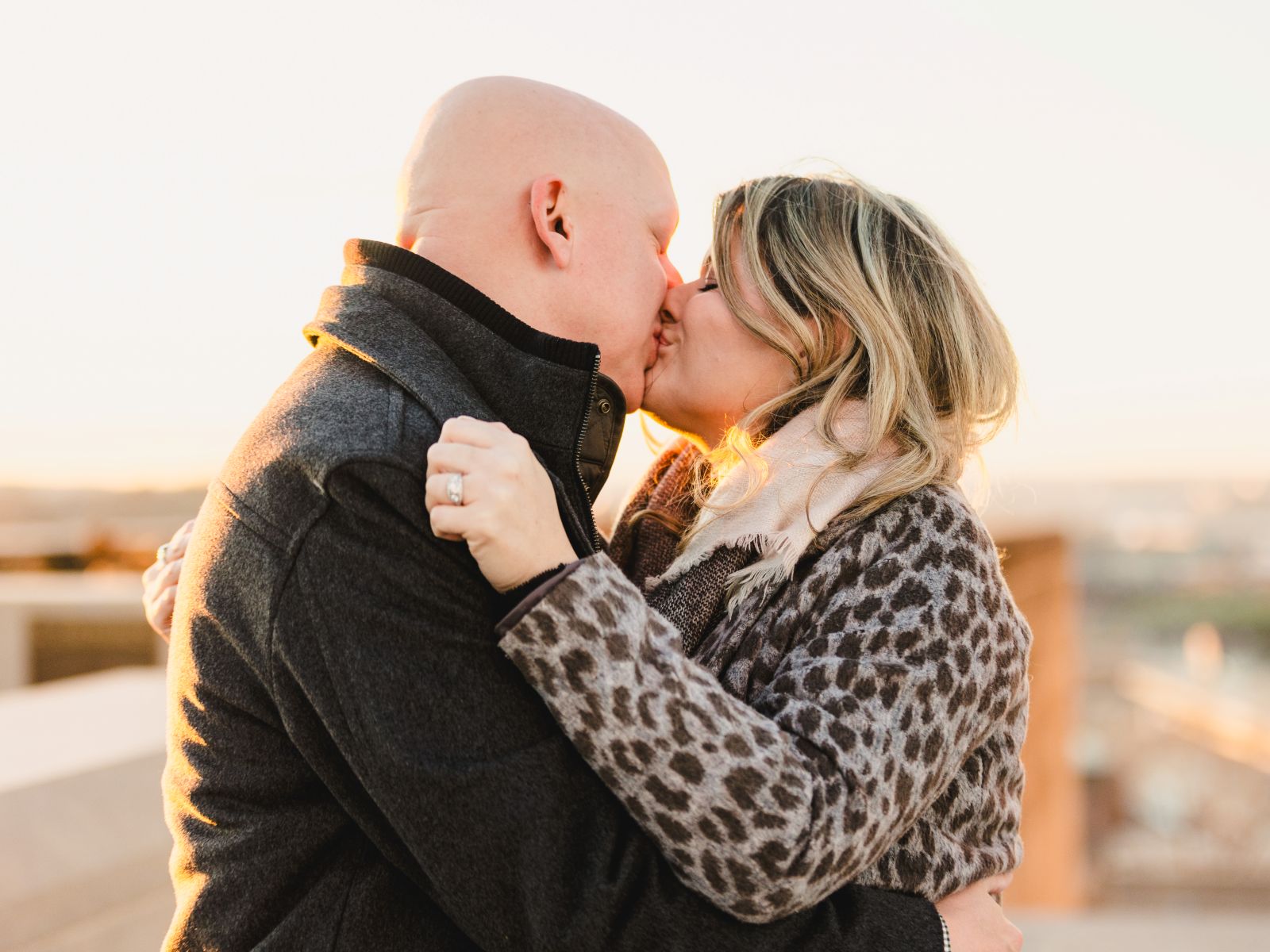a couple kissing at sunset on a rooftop after a man proposed to his partner