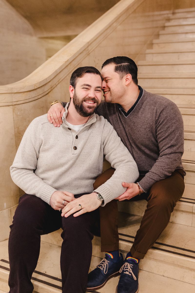 a couple sitting on the steps in a museum after one partner asked the other to marry them
