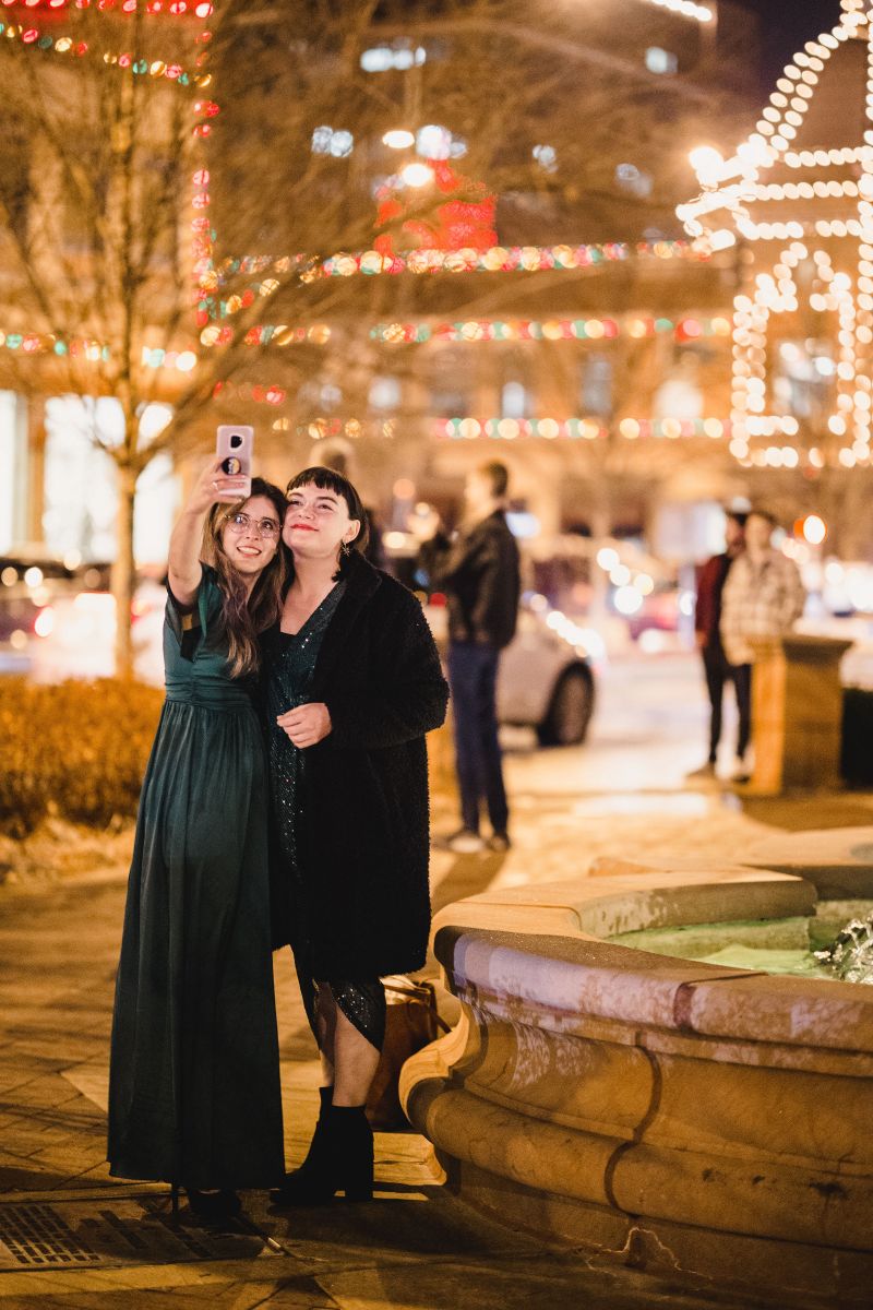 a couple taking a selfie surrounded by christmas lights and next to a fountain