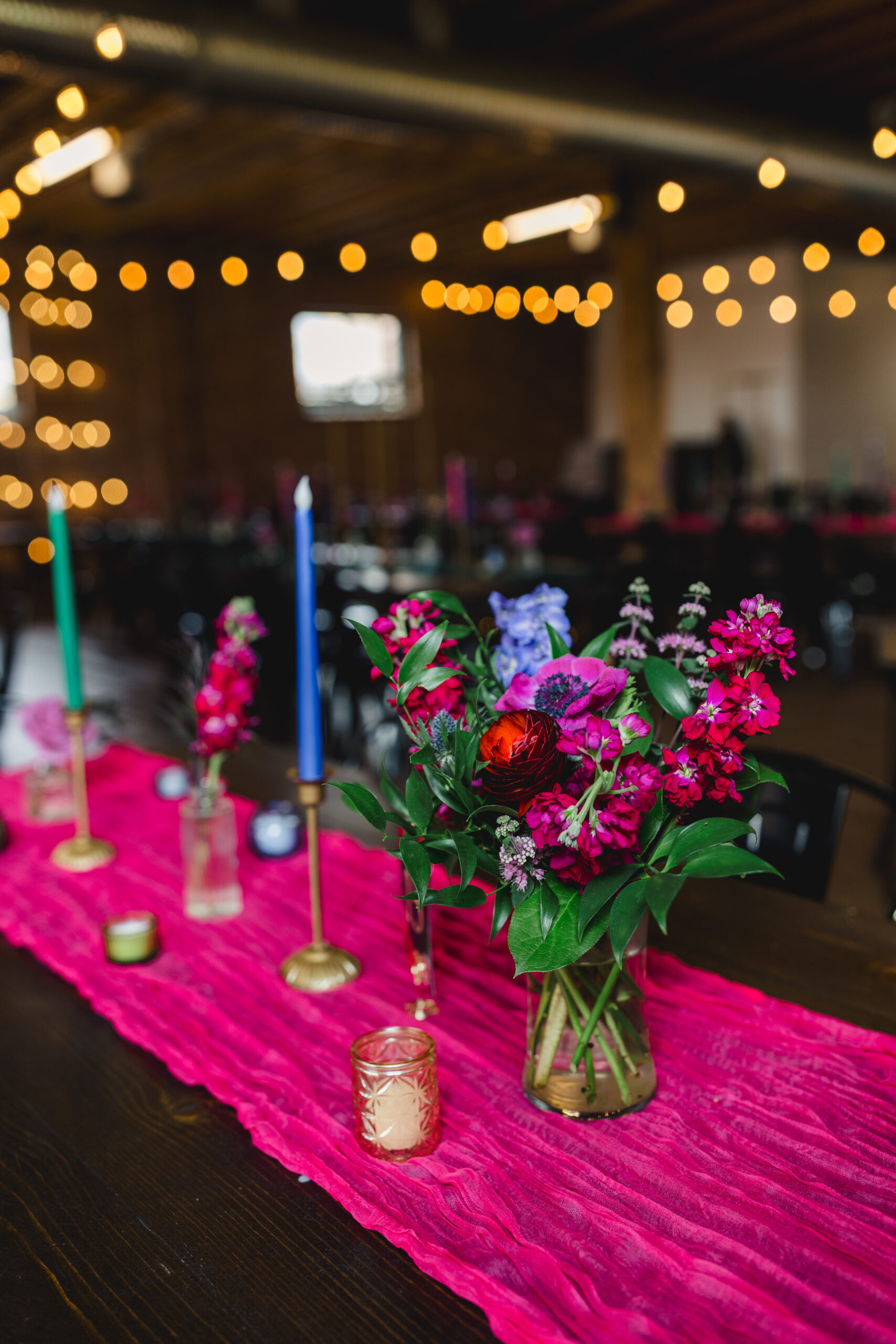 a table set up for a wedding reception inside of union in kansas city the table has on top of it a pink tablecloth and blue and green candles and floral arrangements 