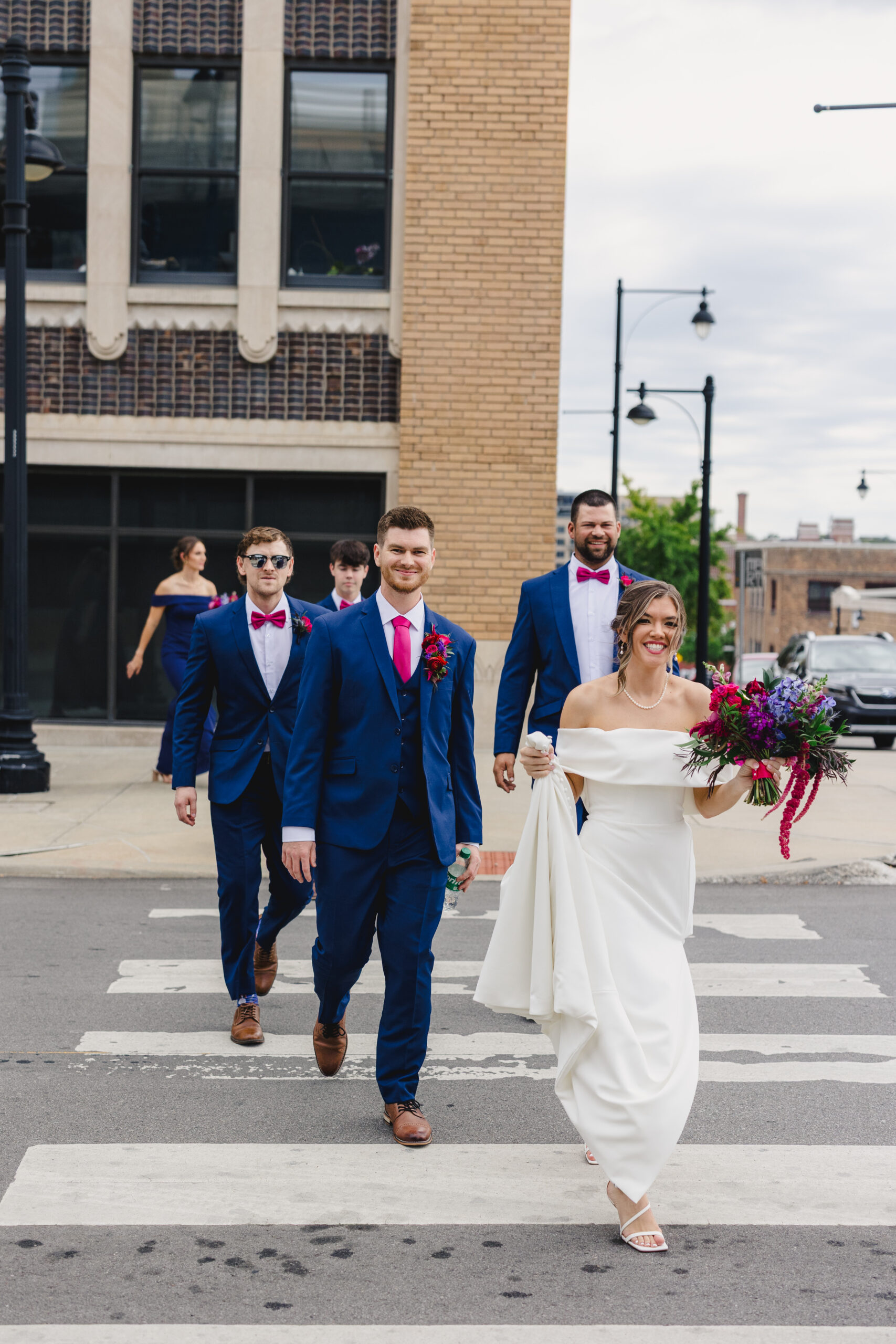 a bride and groom with their wedding party walking across a crosswalk in kansasa city 
