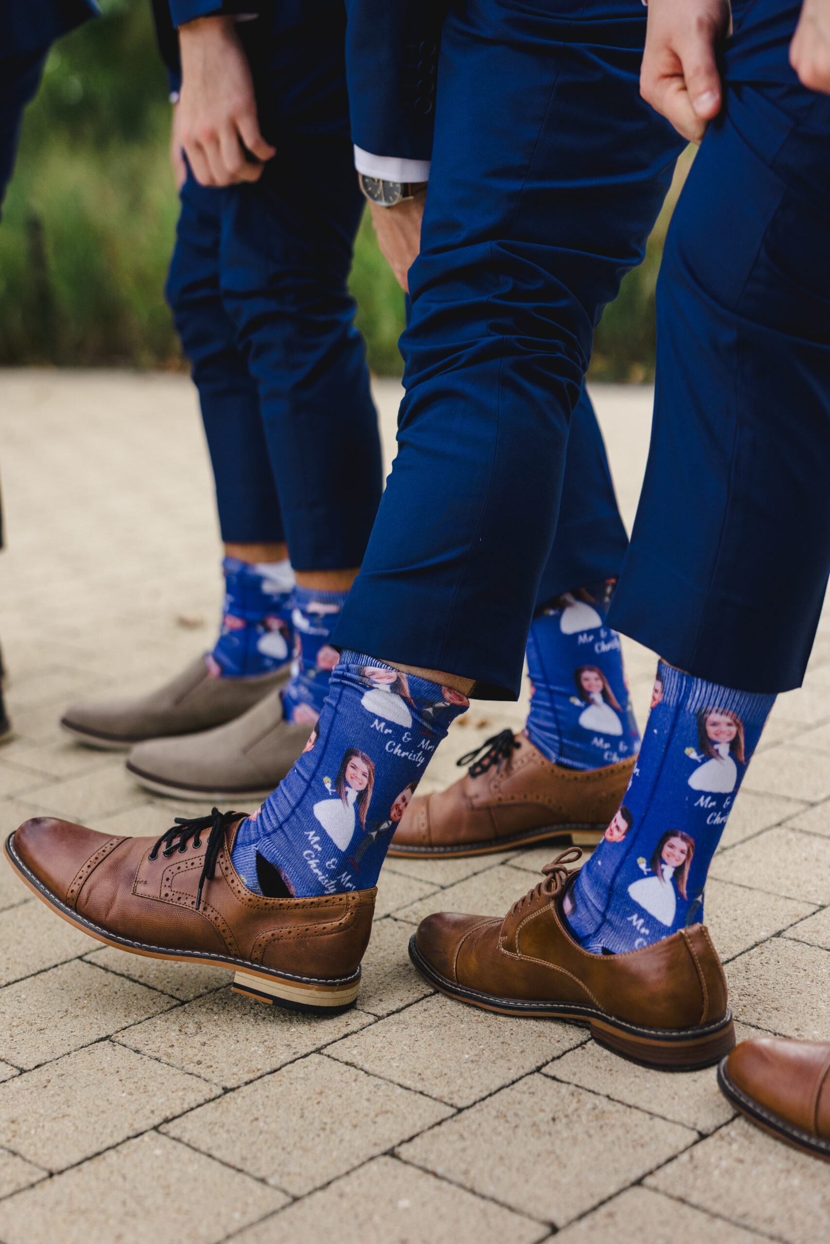 grooms pulling up their pants to show off their matching socks that feature the bride and groom 
