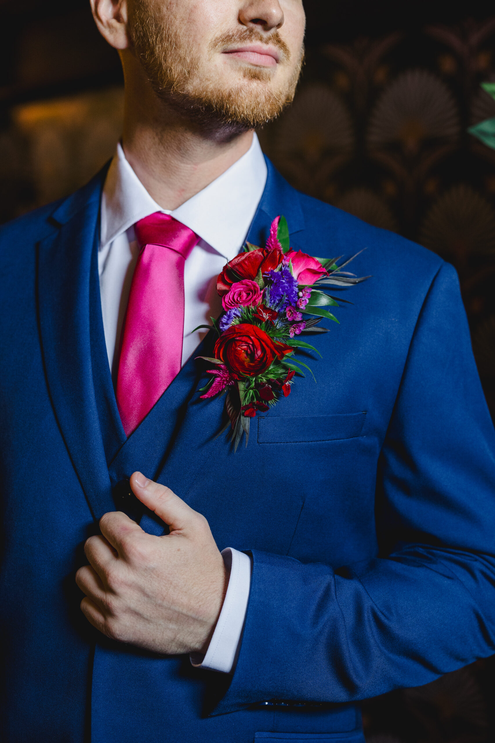 a man wearing a blue tuxedo and pink tie and a boutonniere made up of red and blue flowers 