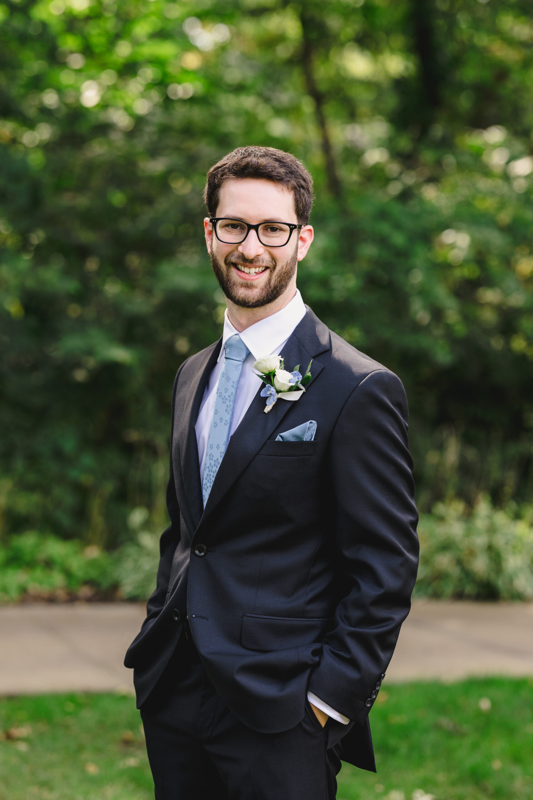 a man smiling on the day of his wedding and taking a solo portrait on a green lawn