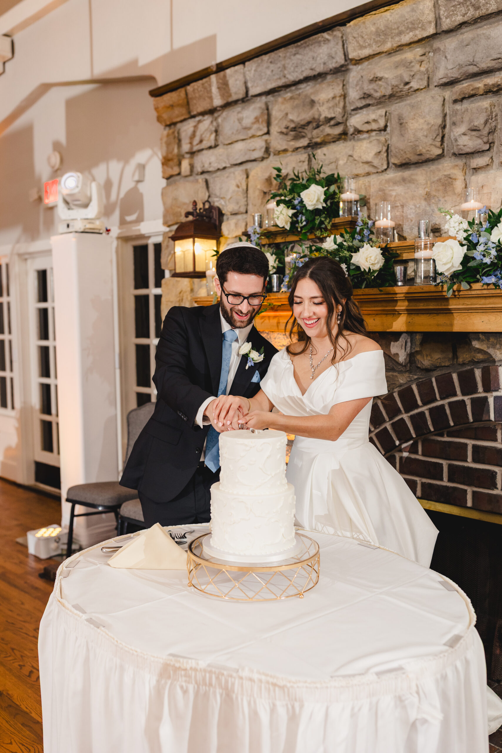 a couple cutting their wedding cake during their reception inside of the elms hotel in kansas city they are cutting their wedding cake next to the fireplace and smiling 
