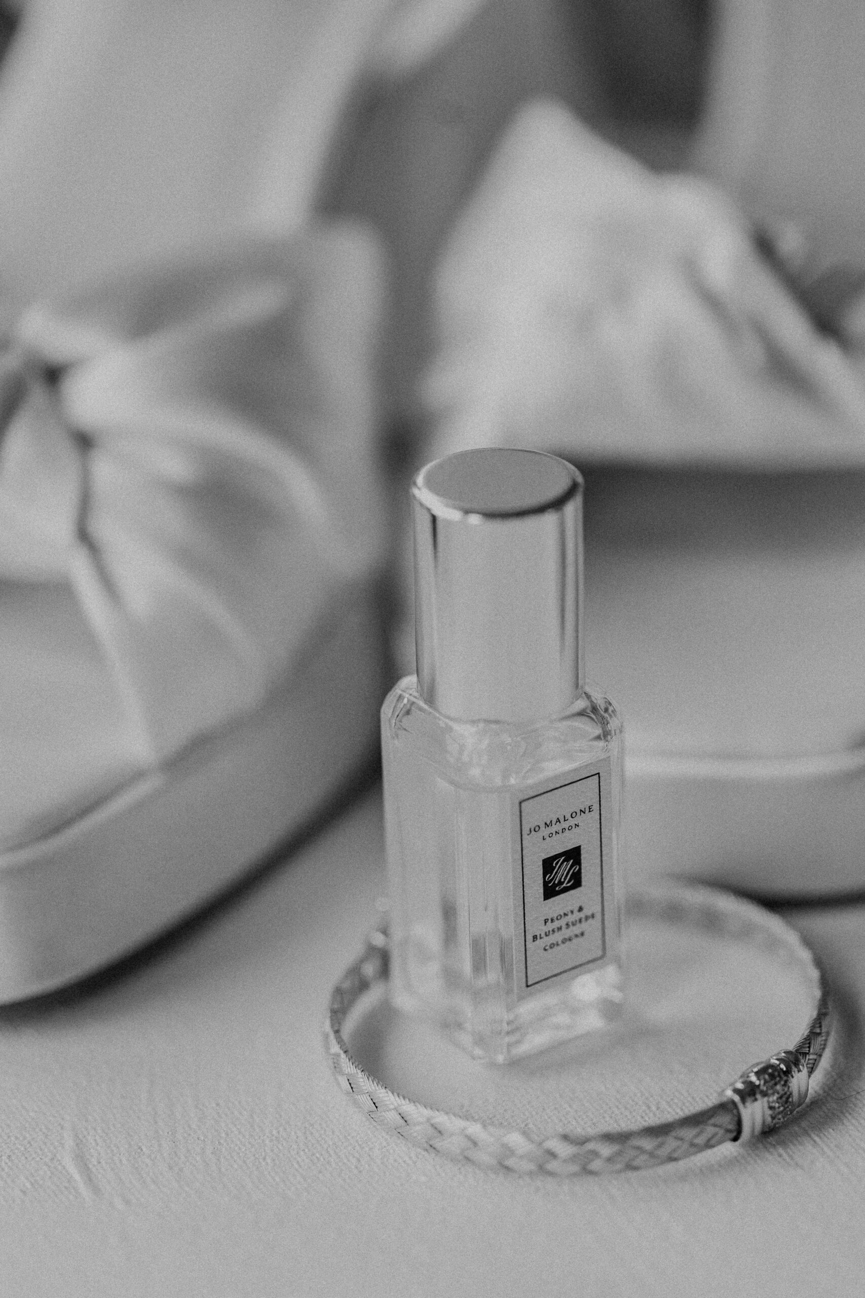 a bottle of perfume, a gold bangle, and a pair of white wedding heels 