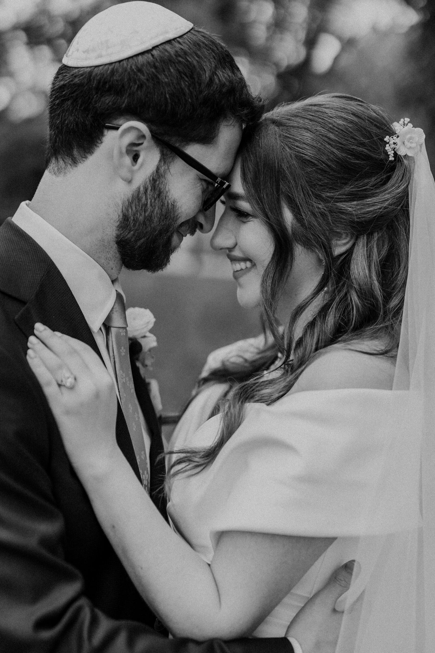 a couple taking a wedding couples portrait they have their heads pressed together and are smiling at each other the man is wearing a kippah 