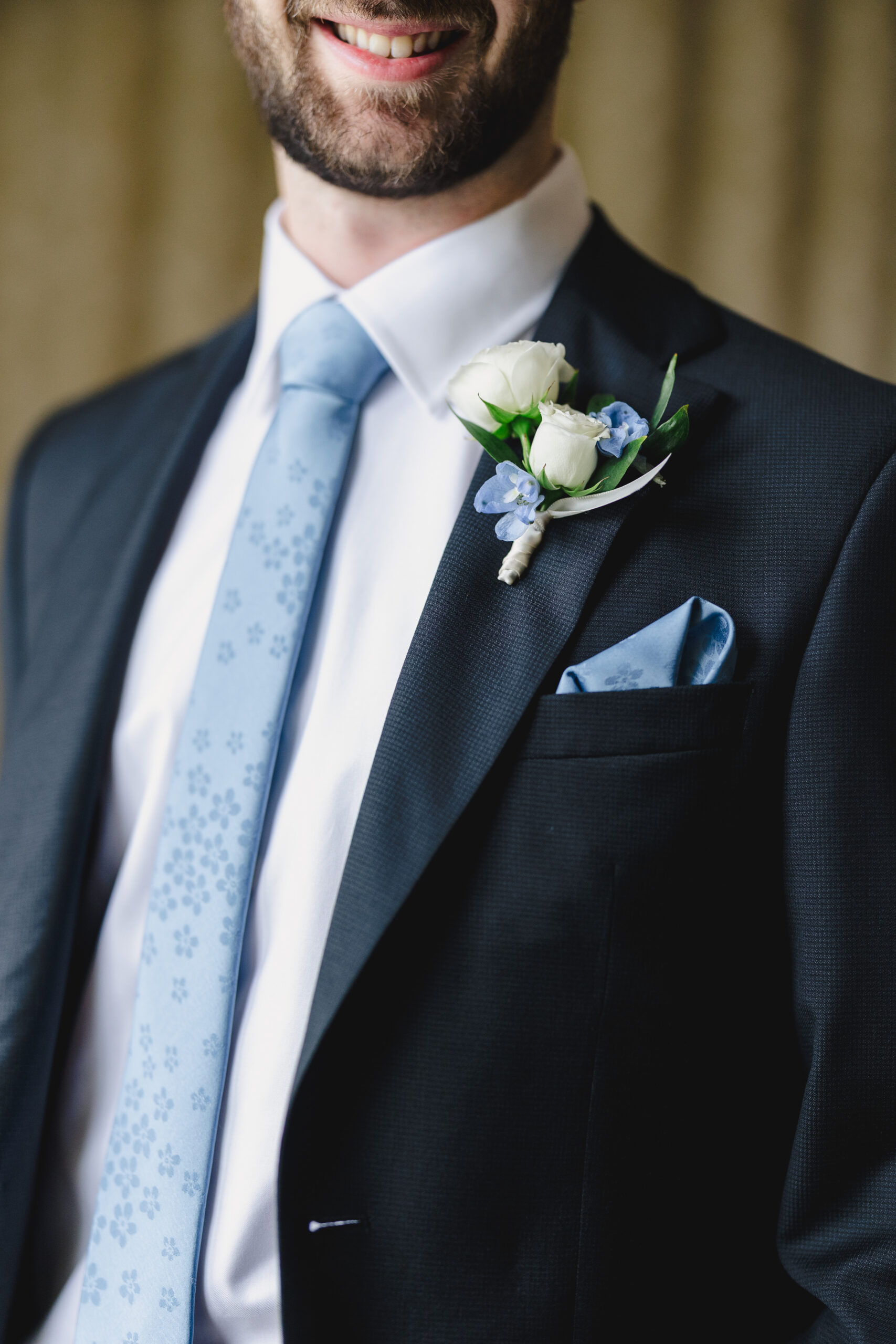 a close up shot of a groom wearing a blue tie and boutonniere with white and blue flowers 