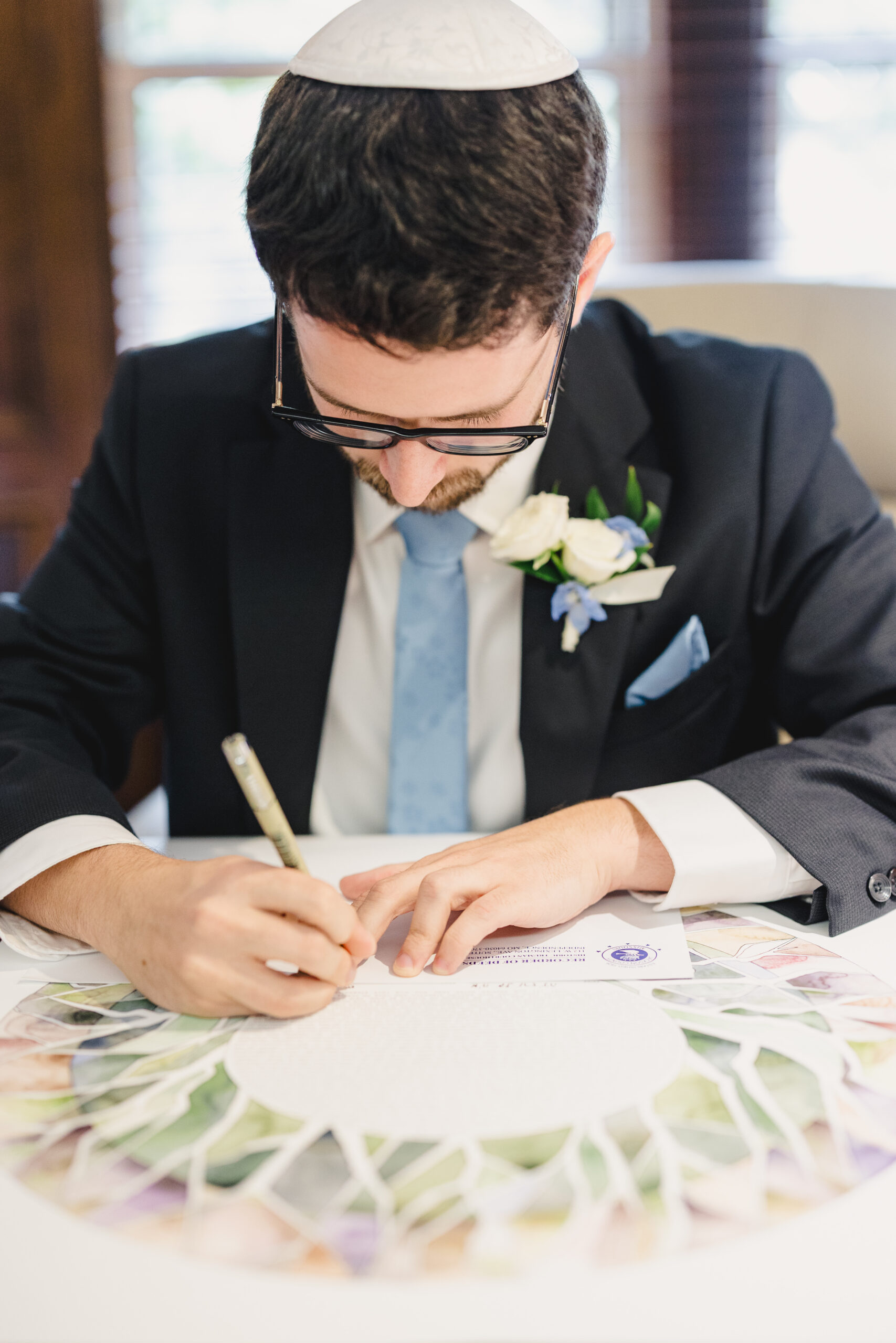 a groom wearing a kippah signing his wedding certificate 