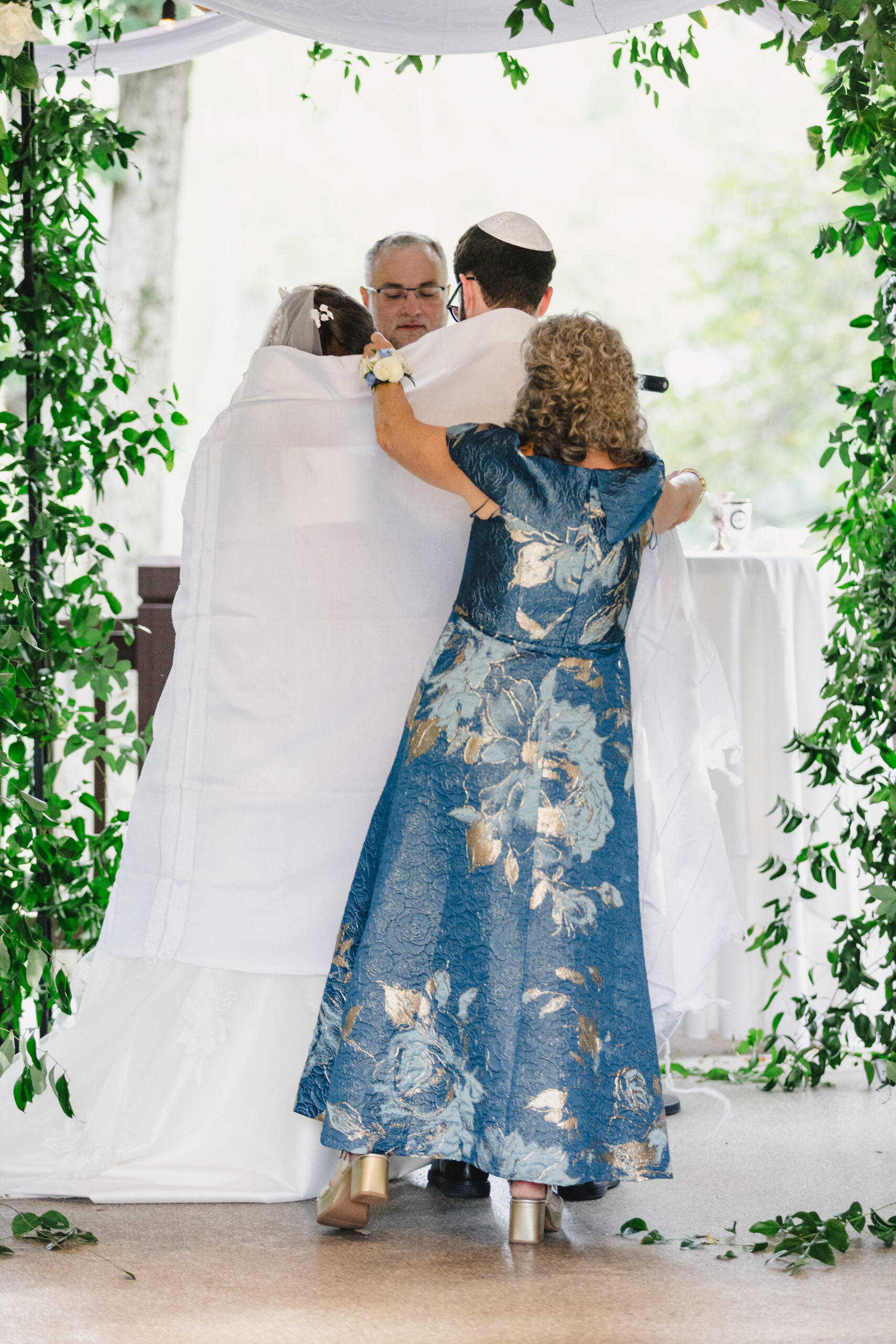 a couple having their wedding ceremony inside of a gazebo the bride's mother is covering the bride and the groom with a white blanket 
