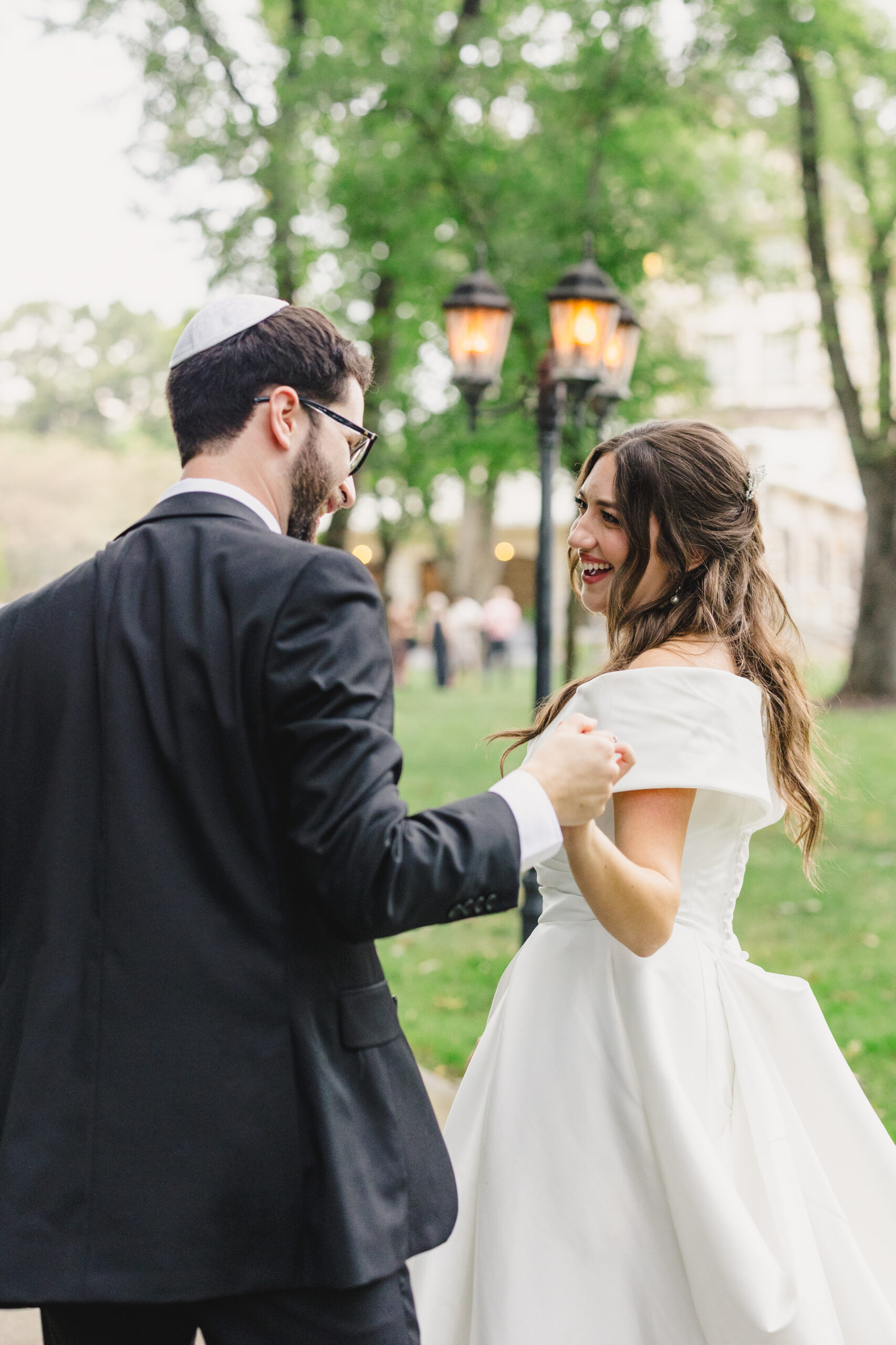 a couple walking along a paved path next to a lampost holding hands and laughing with one another 