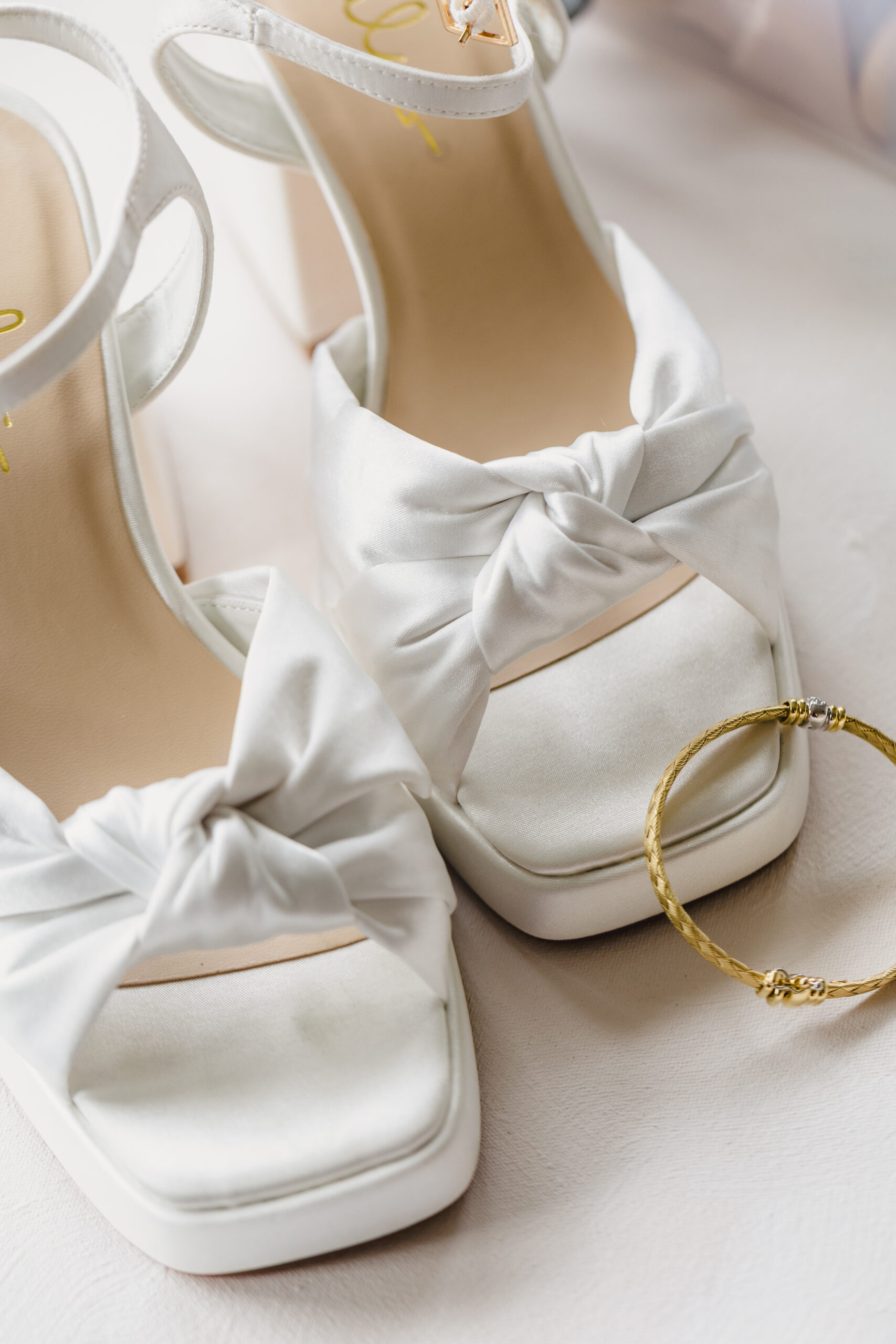 a pair of white wedding hands with a gold bangle propped against one shoe 