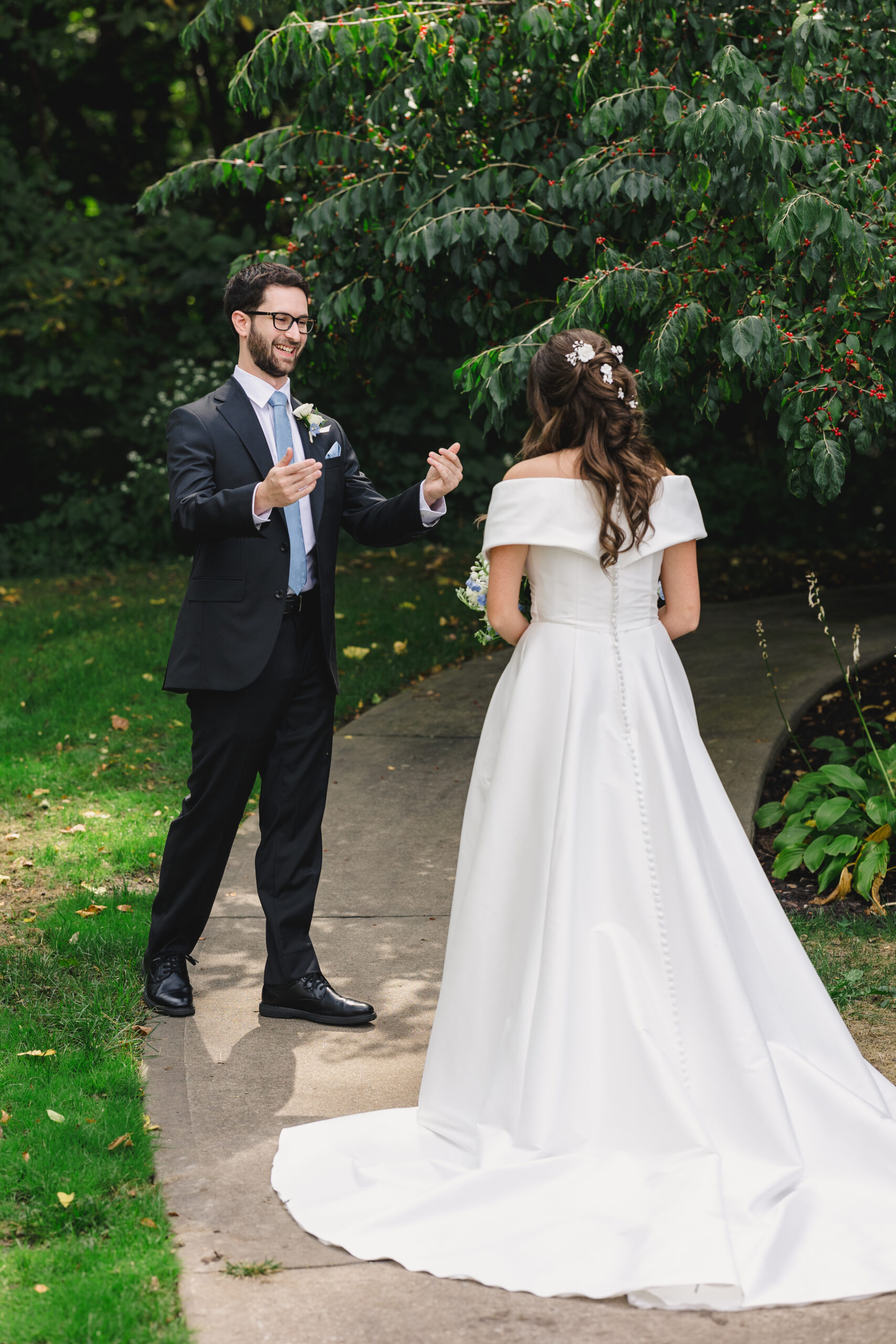 a couple sharing a first look on their wedding day the woman is wearing a white wedding dress and the man is welcoming her towards him and is wearing a black suit 