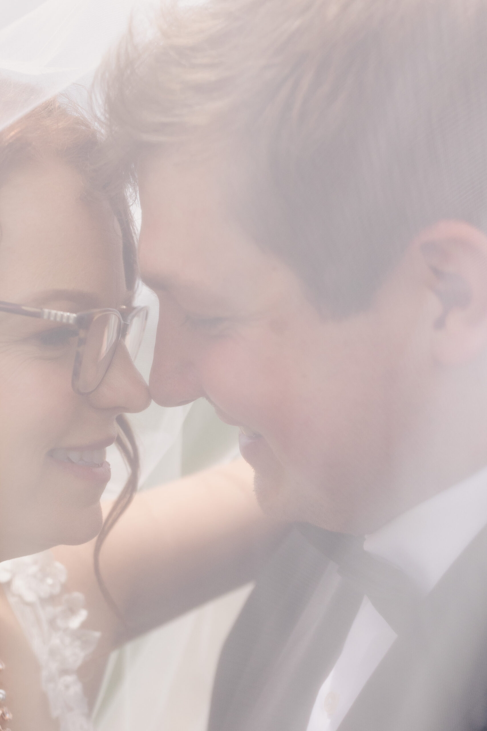 a couple smiling at each other underneath of the bride's veil 