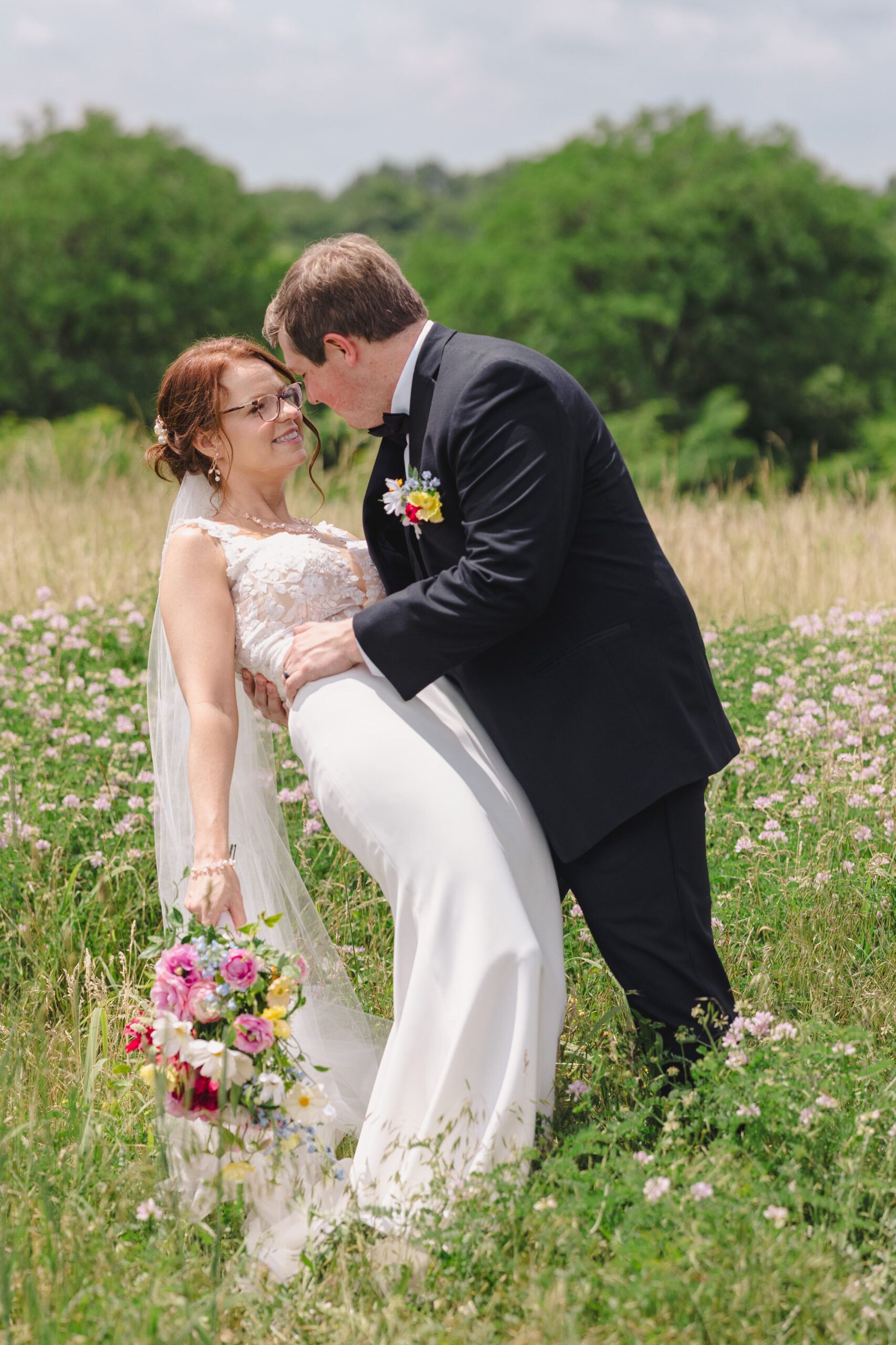 a man dipping his bride backwards in a field 