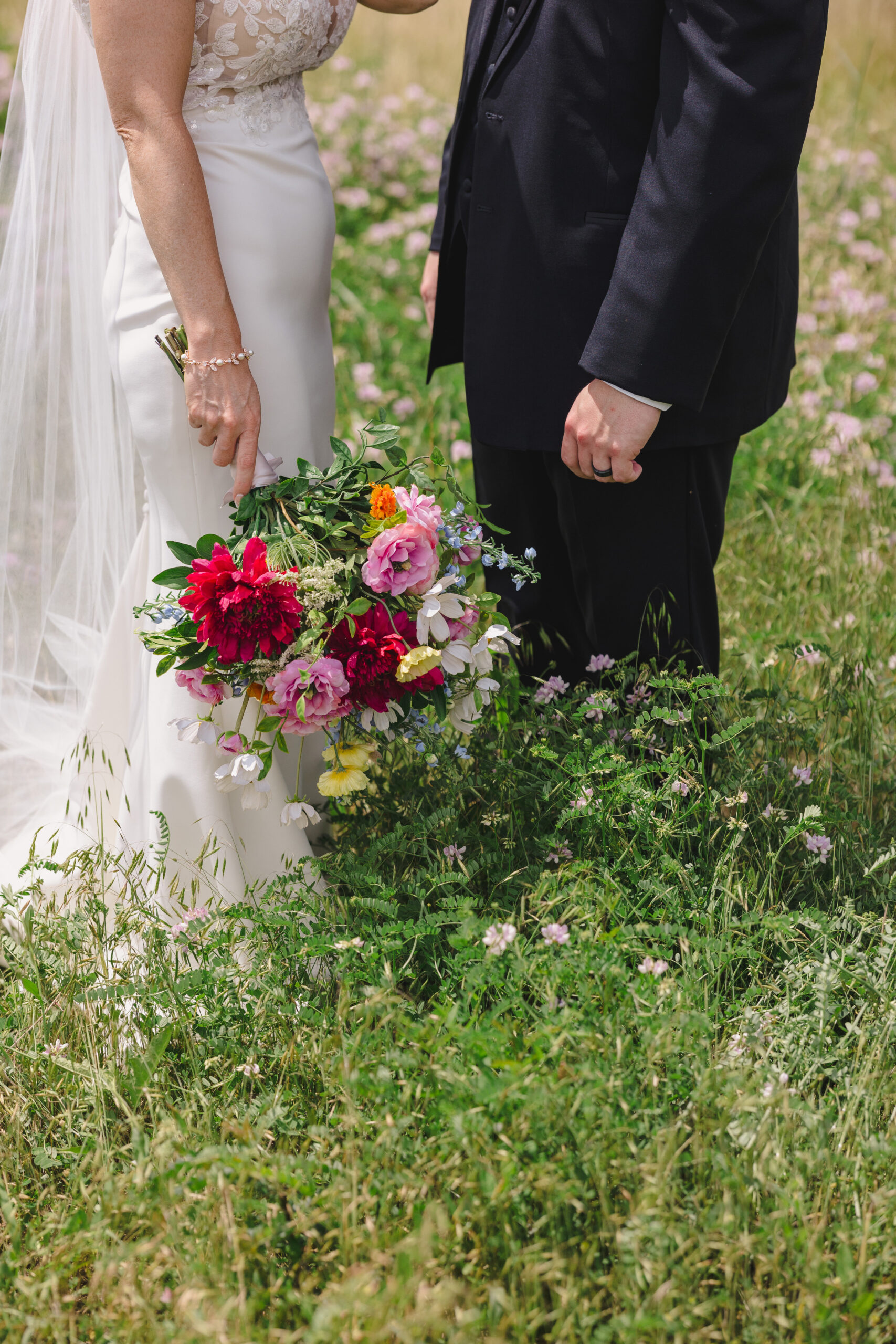 a couple standing together in a field while the woman olds a bouquet of flowers in her hand 