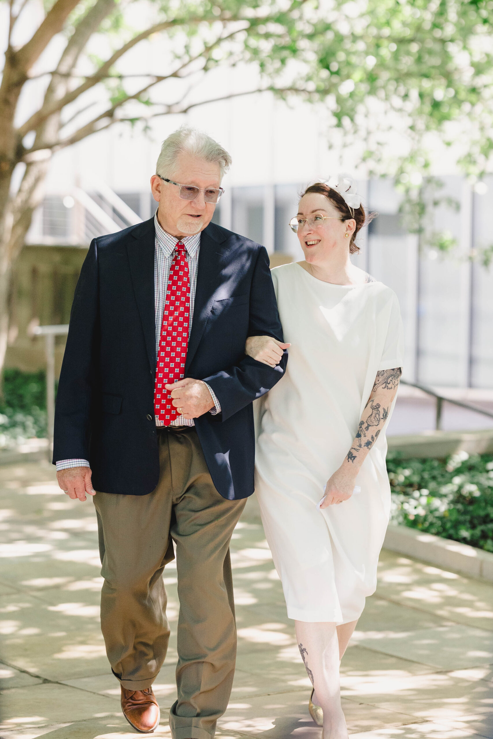 a woman walking arm in arm down a sidewalk with her dad on the day of her wedding 