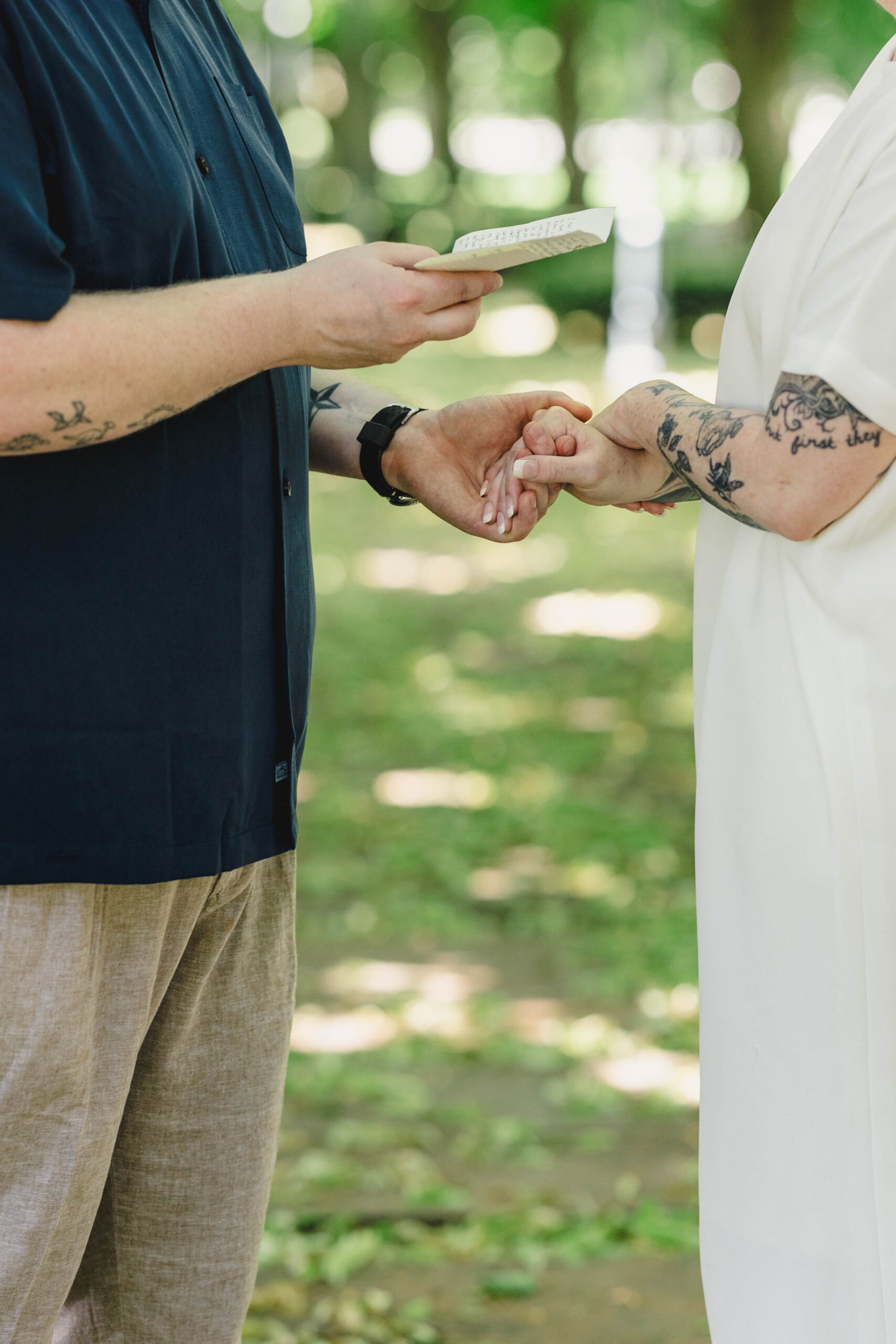 a groom holding his bride's hand and reading private vows to her on the grass 