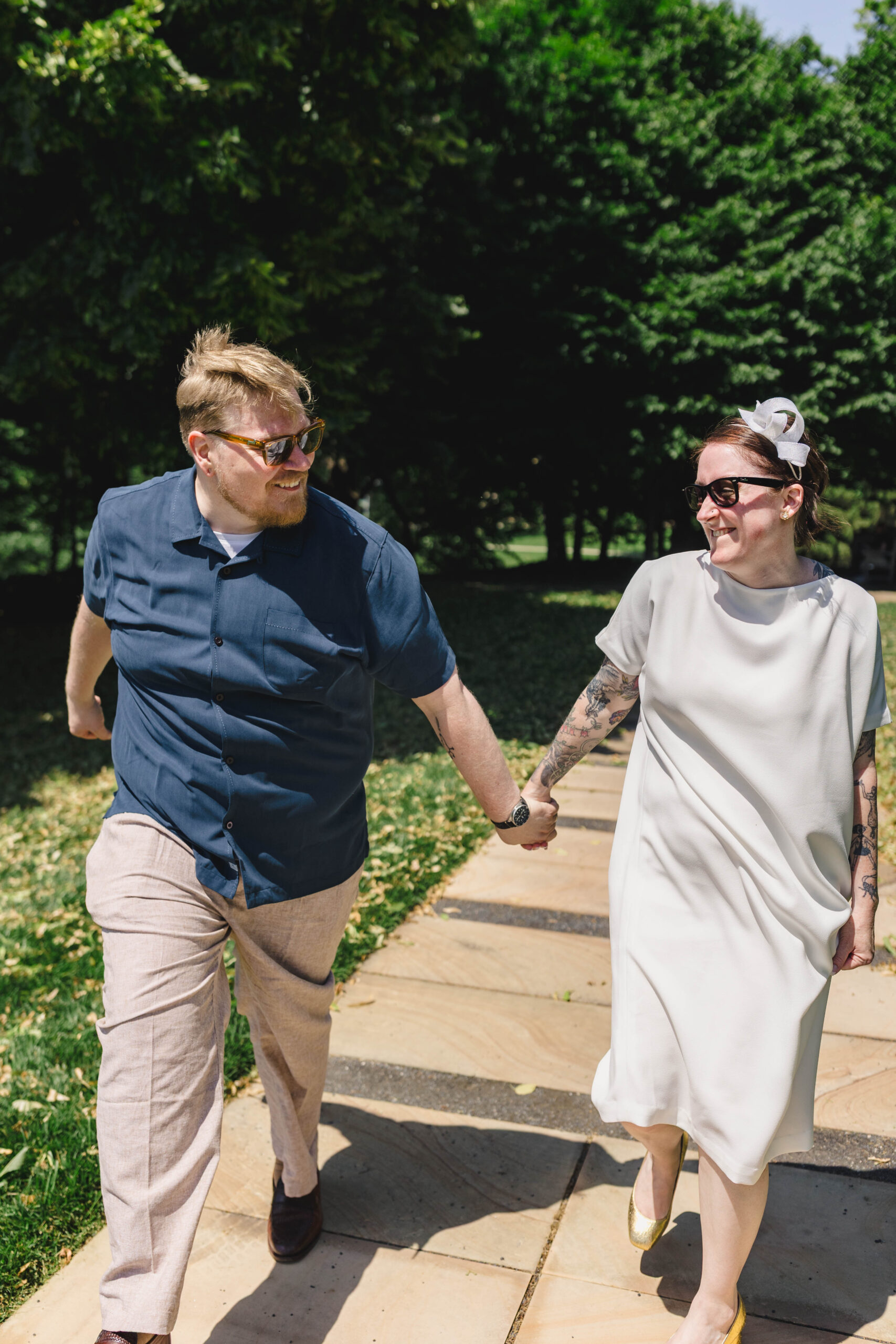 a couple walking hand in hand down a sidewalk smiling at each other and wearing sunglasses 