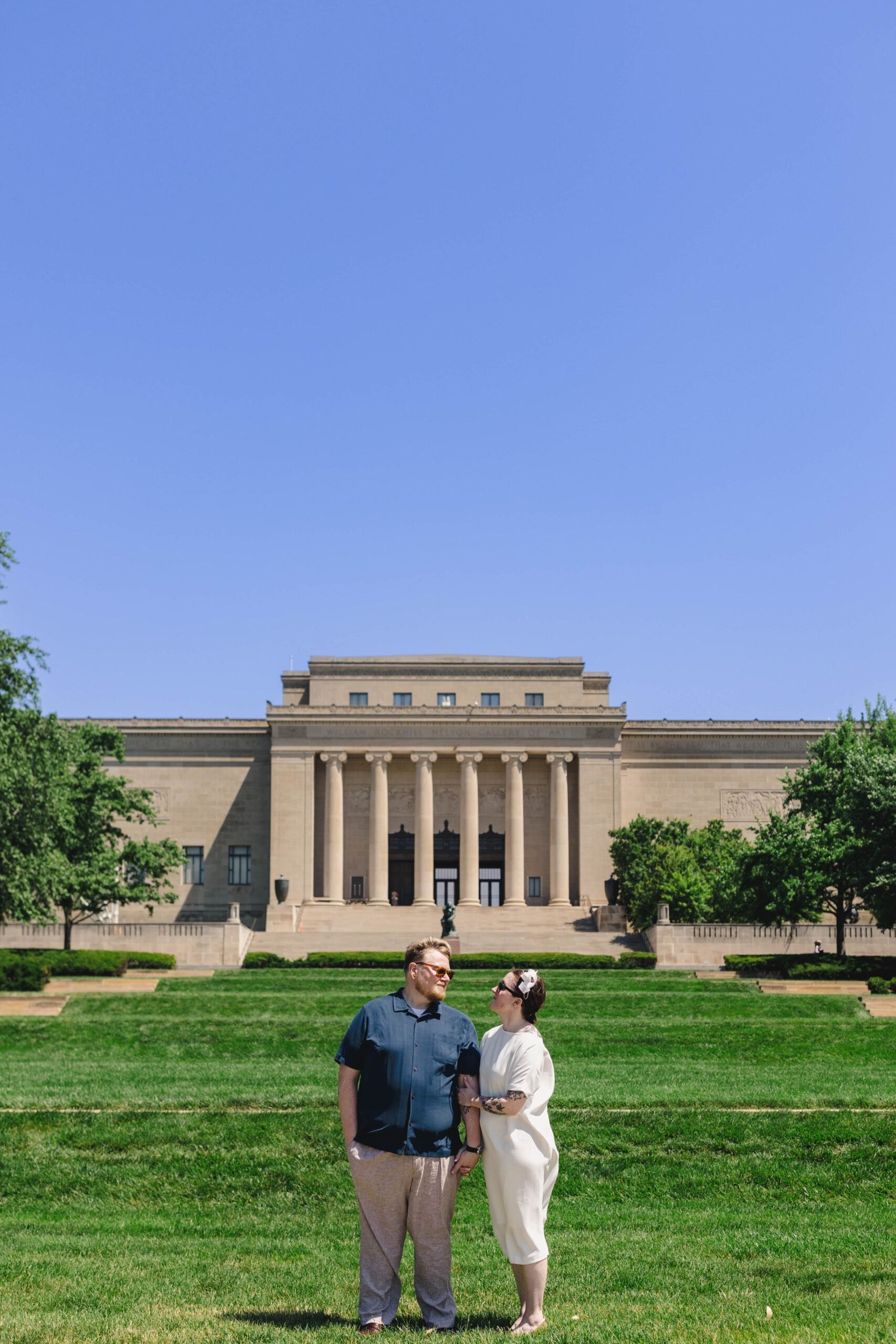 a couple taking pictures on the lawn of the nelson atkin's museum after their wedding ceremony 