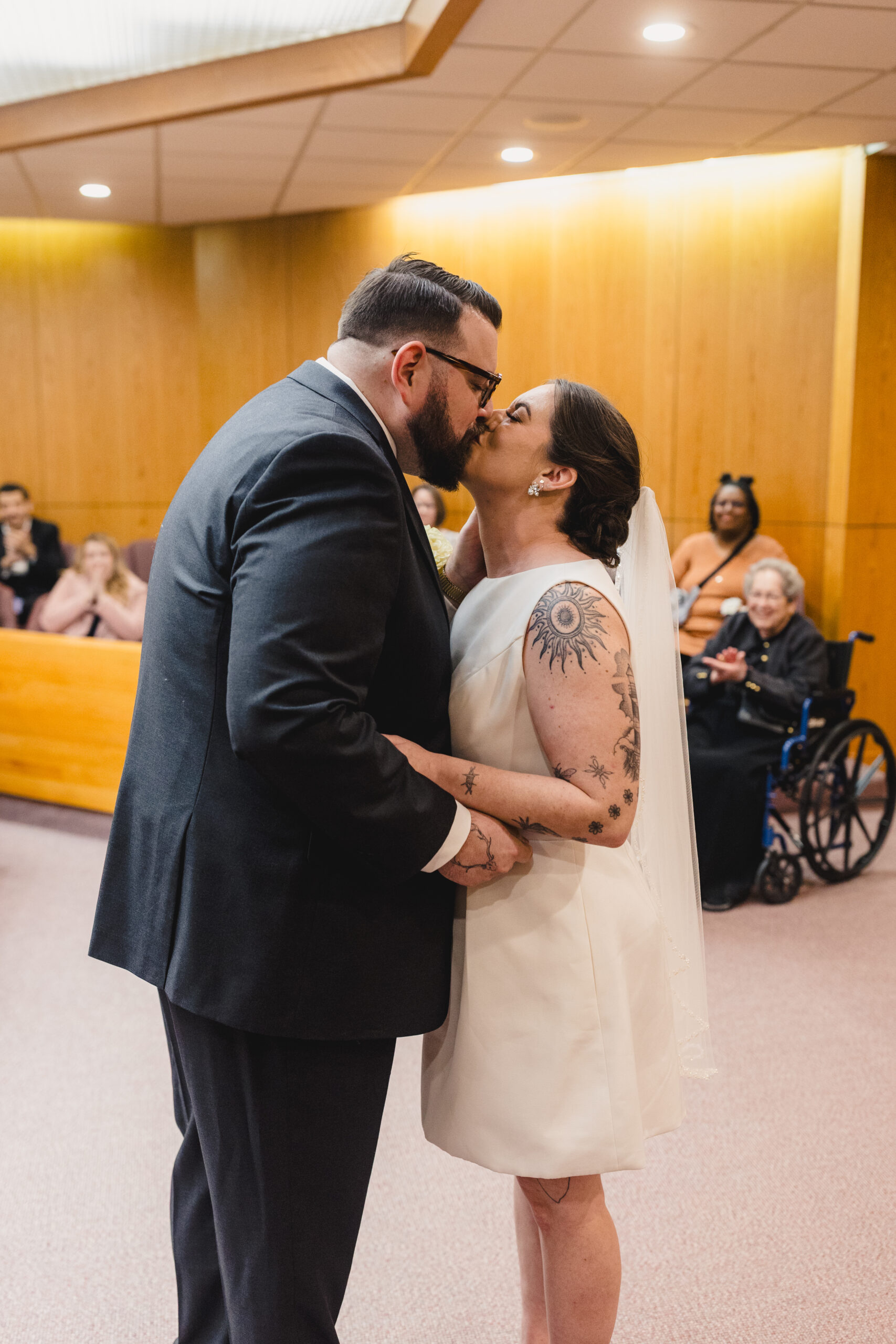a bride and groom kissing in the courthouse during their wedding ceremony as their guests watch