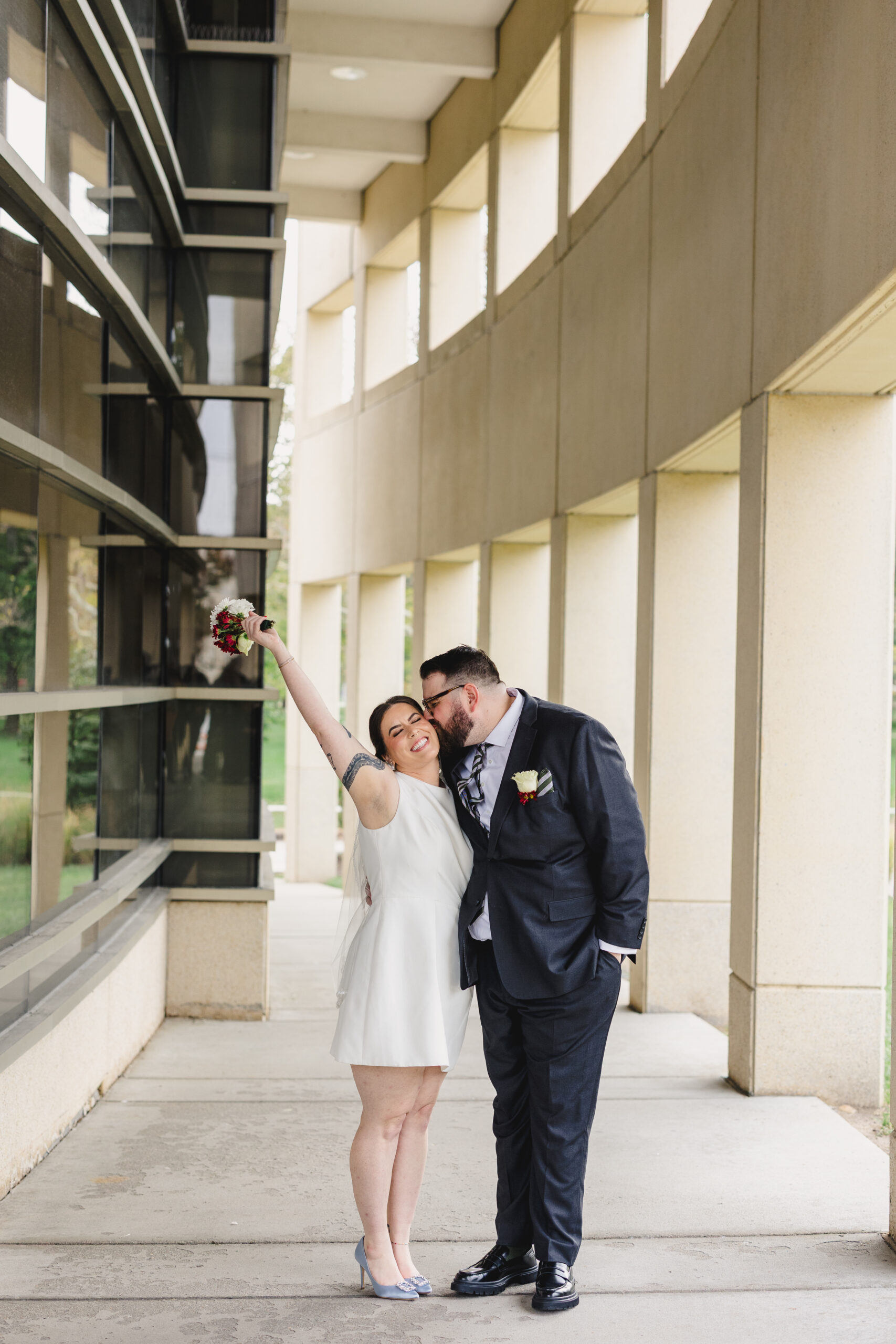 a man kissing his bride on the cheek on the day of their wedding the woman is wearing a short white dress and holding her bouquet up in the air 