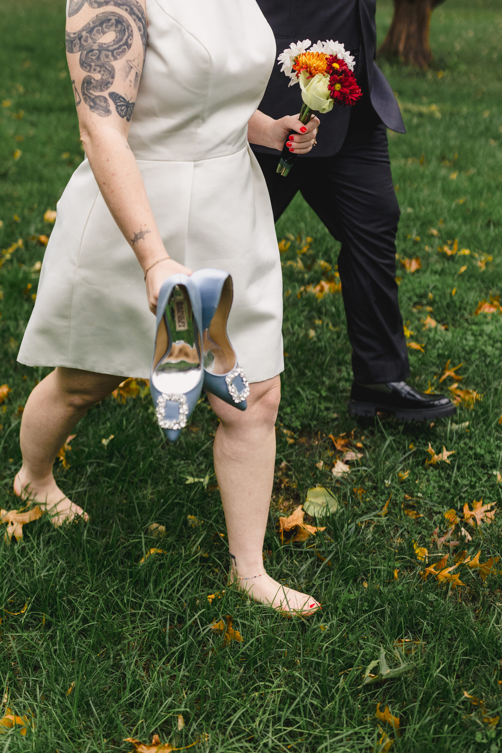 a bride and groom walking through the grass together the bride in carrying her heels in her hand 