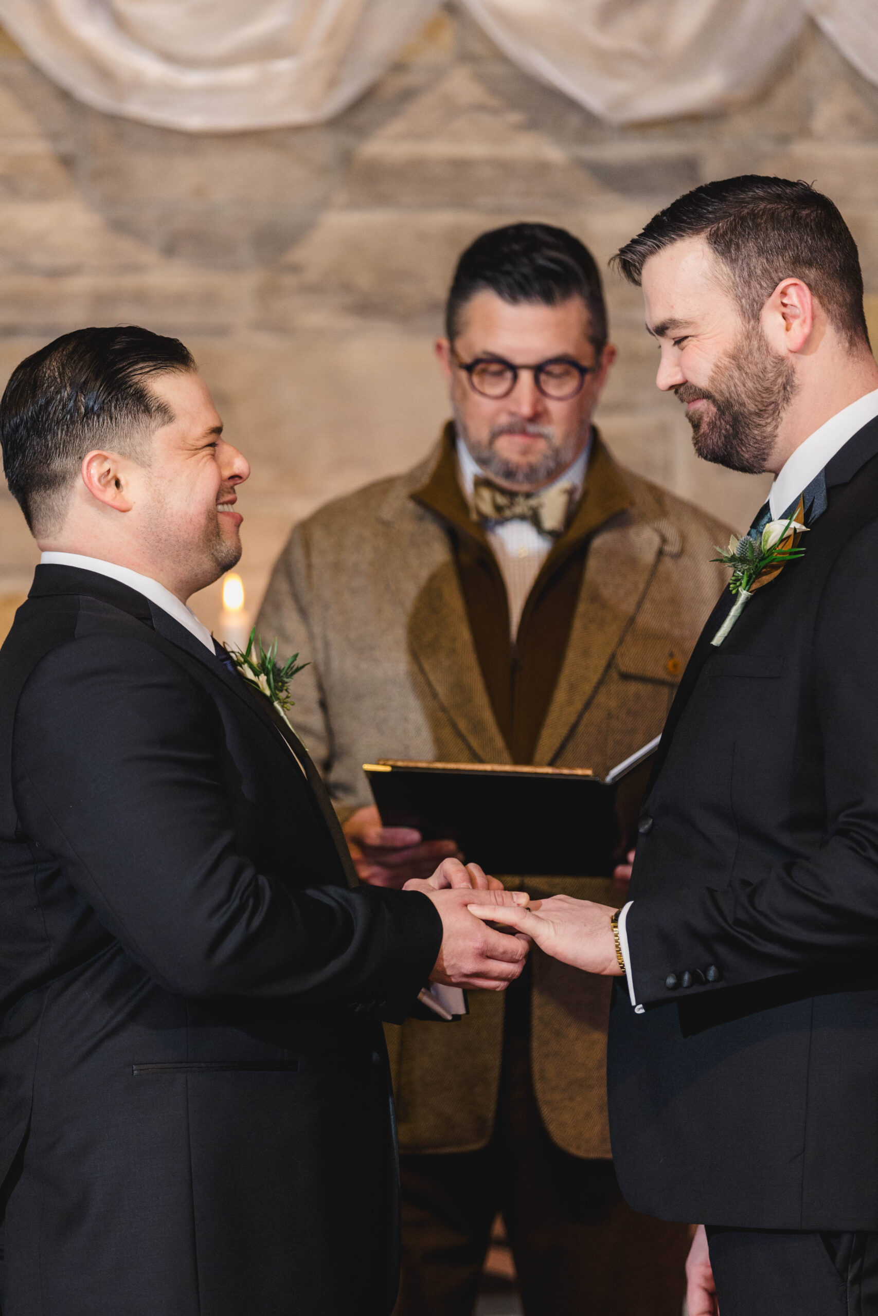 two men at their wedding ceremony in a church one man is placing a ring on his partner's hand in front of their officiant 