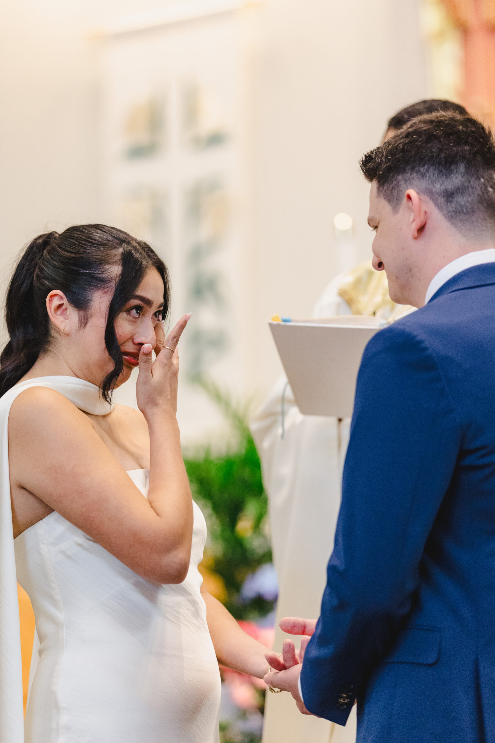 a bride and groom looking at each other during their wedding ceremony as the bride wipes tears from her eyes 