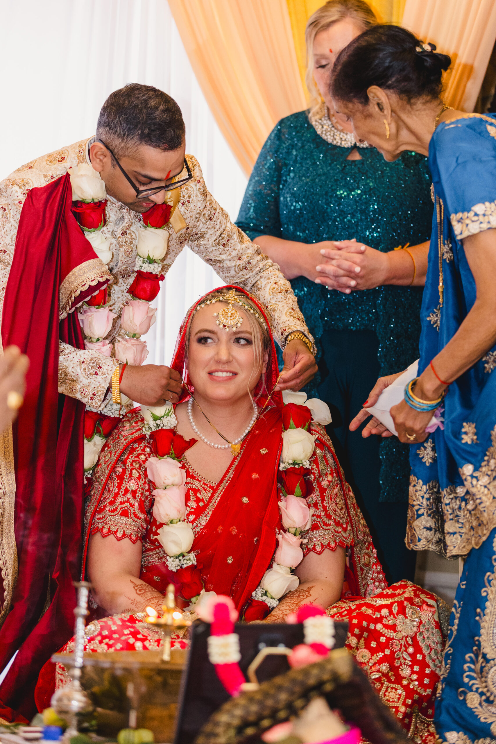 a woman sitting at her wedding ceremony as her partner places a garland around her neck 