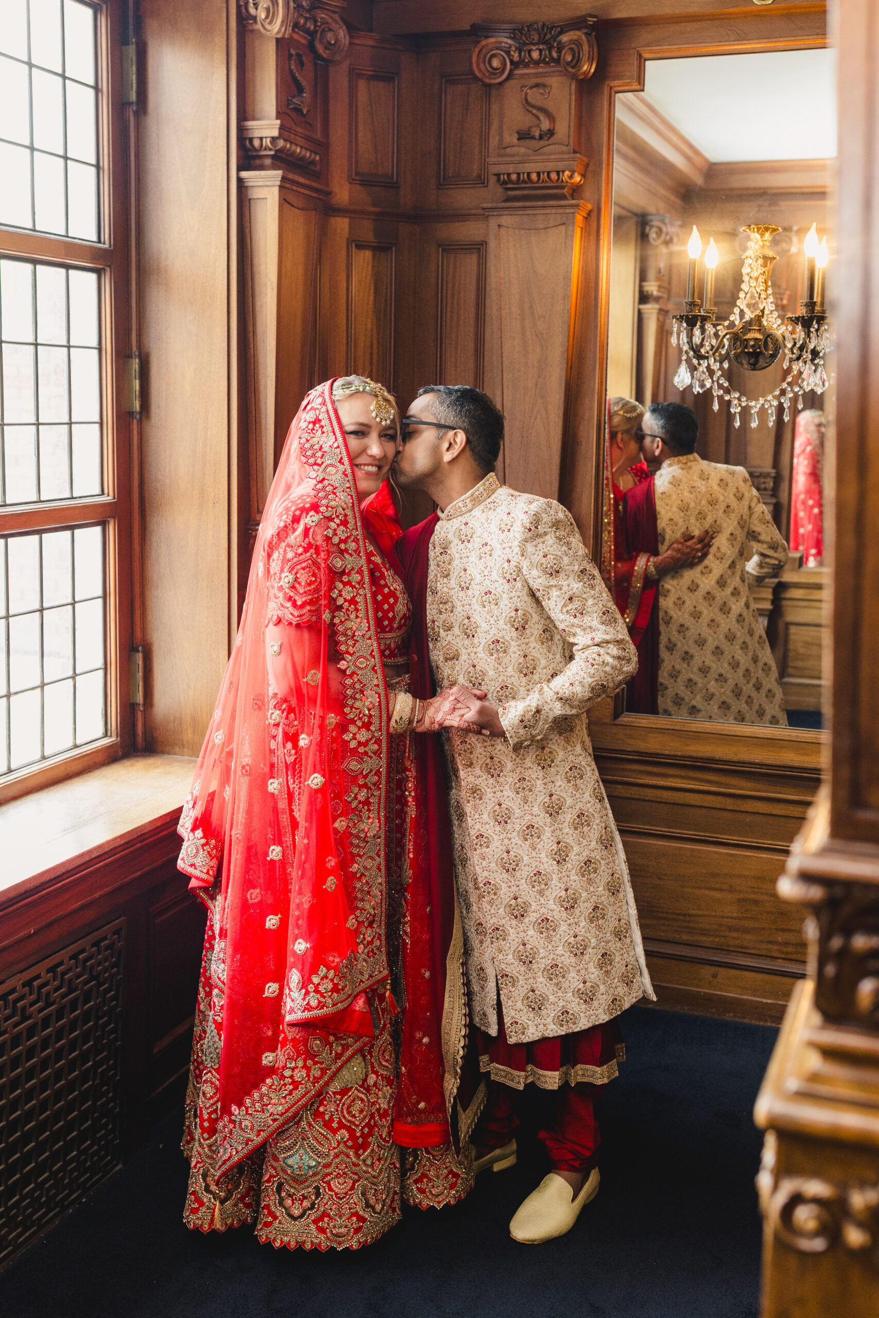 a couple taking wedding portraits inside of loose mansion the man is holding his bride's hand and kissing her on the cheek 