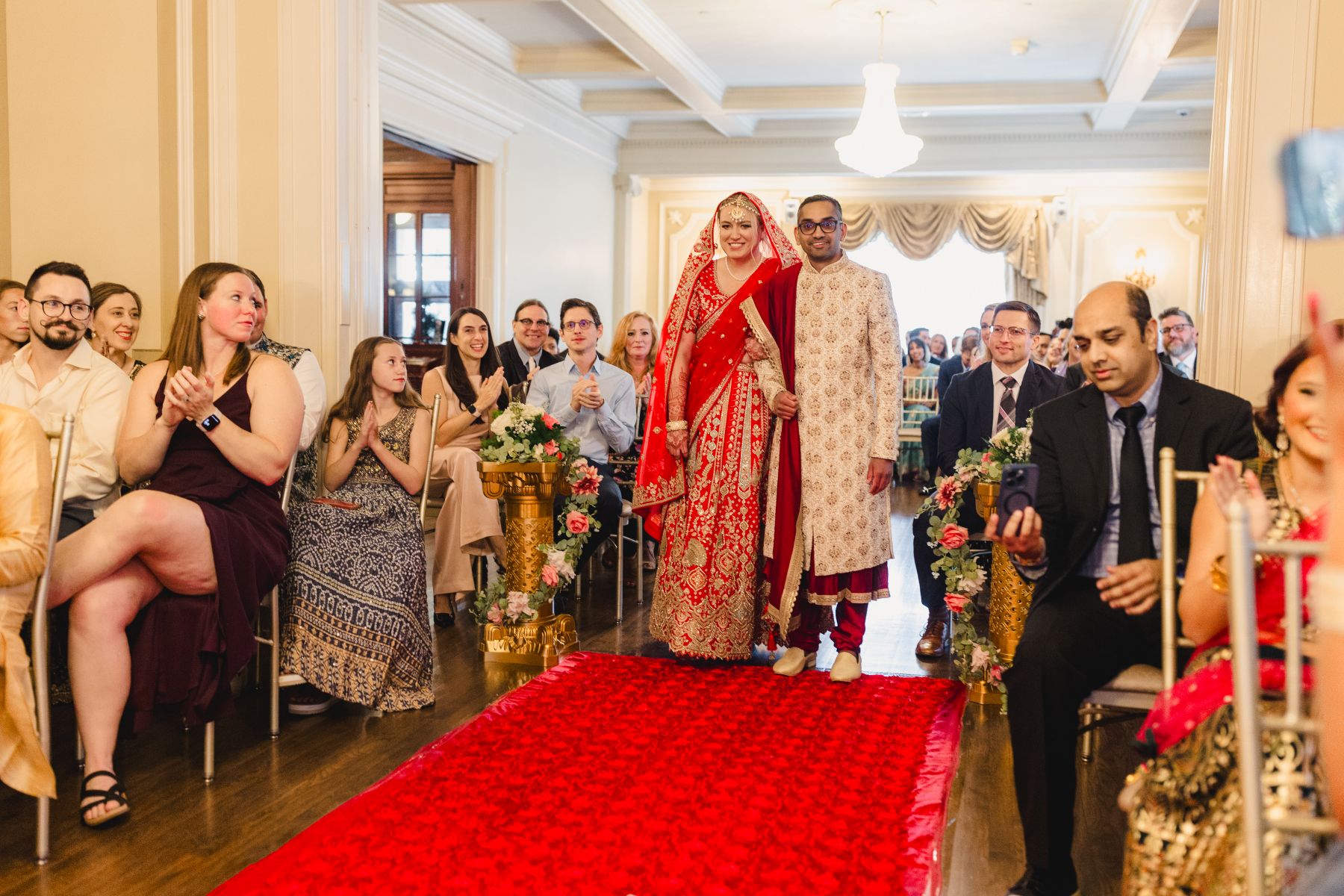 a couple walking arm in arm down a red carpet for their wedding ceremony inside of loose mansion 