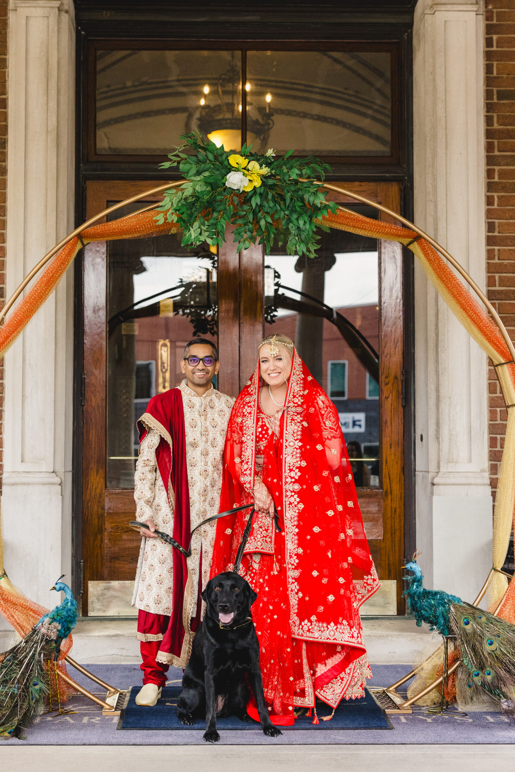 a couple with their black lab taking a photo in front of loose mansion in kansas city 