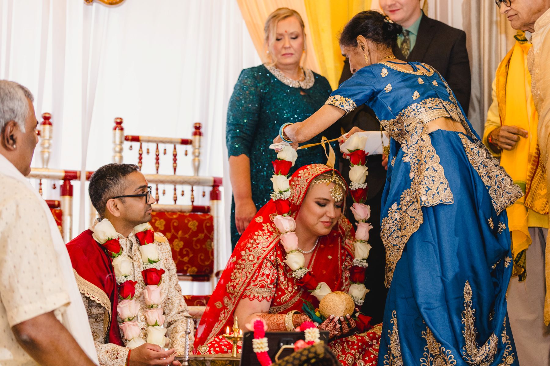a woman placing a garland of roses on the bride during a traditioanl indian wedding ceremony