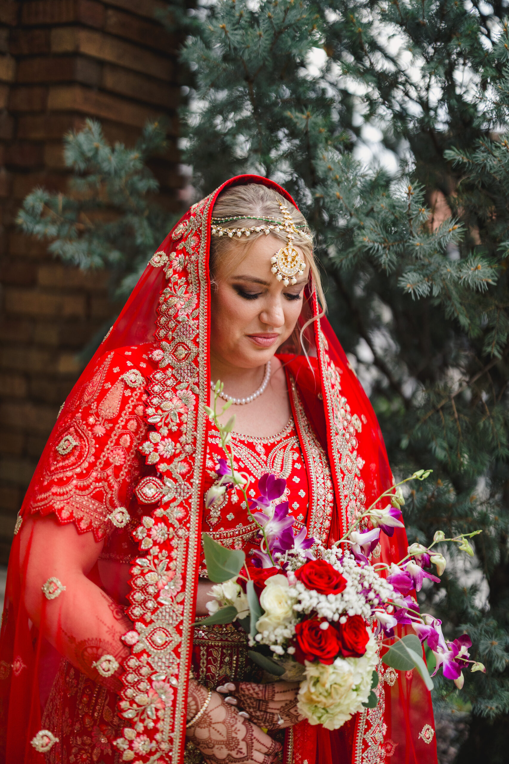 a bride dressed in traditional indian attire holding a bouquet of flowers and looking down at them 