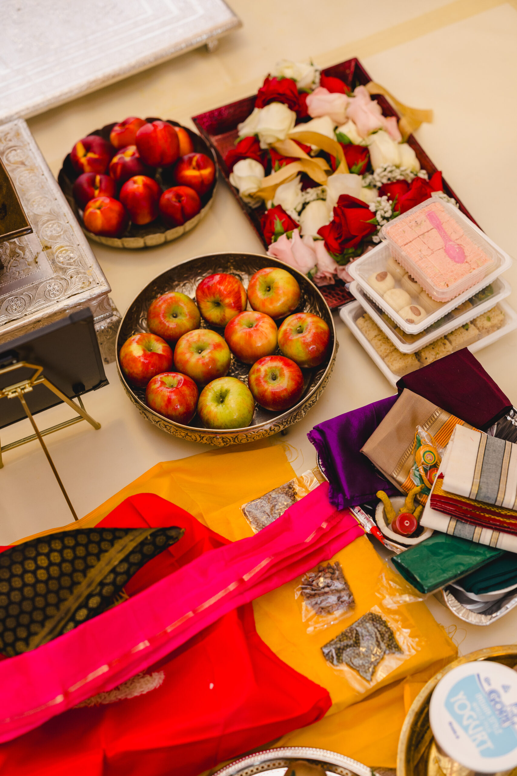 a variety of objects includes shawls, roses, and apples on the ground for a traditional indian wedding ceremony