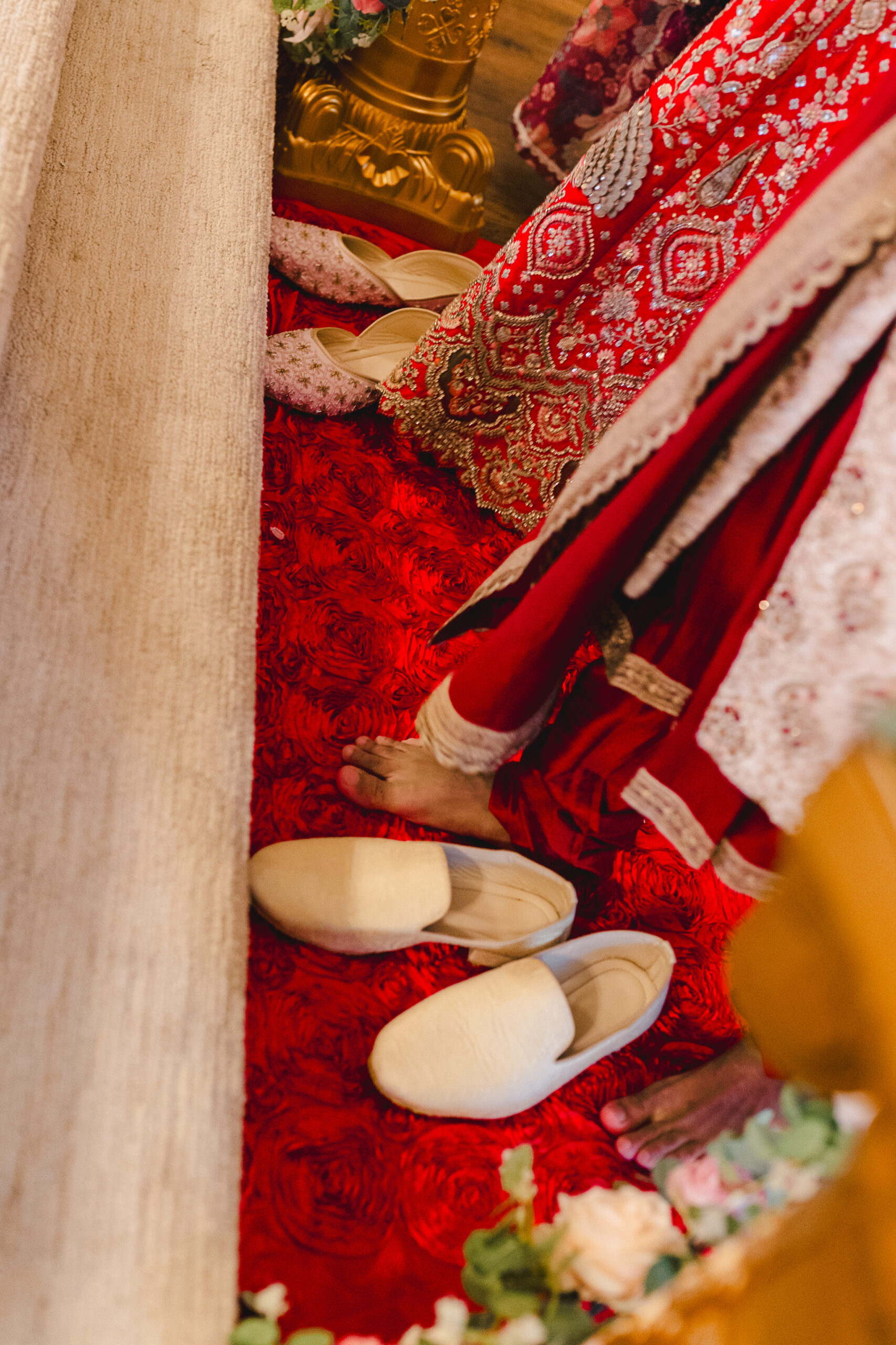 a couple wearing traditional indian wedding attire stepping on red carpet with their shoes next to them 