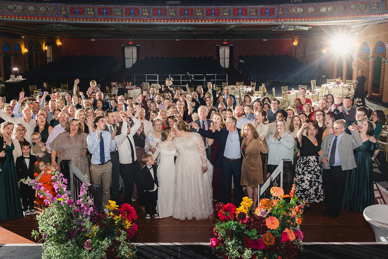 two brides with their wedding guests taking a group photo inside the uptown theater in kansas city 