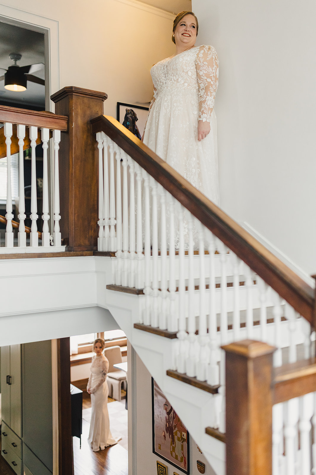 two brides standing on different floors of an airbnb both wearing white wedding dresses 