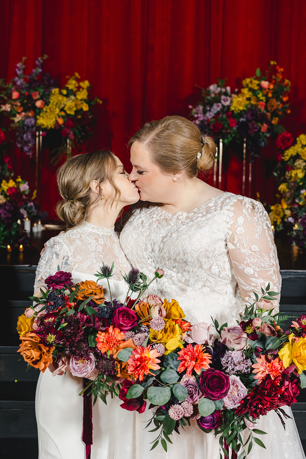 two brides kissing inside of the uptown theather in kansas city after their wedding ceremony they are both holding bouquets of flwoers 