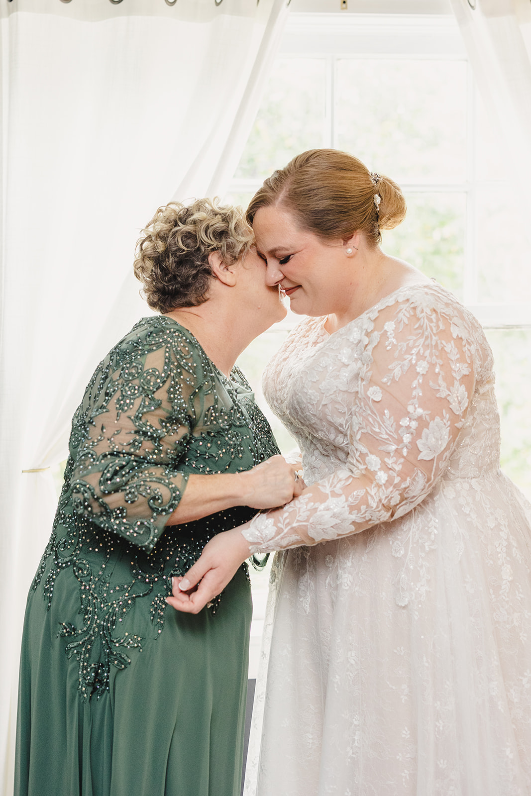 a mother and a bride together the mother is leaning in to kiss the bride on the cheek 