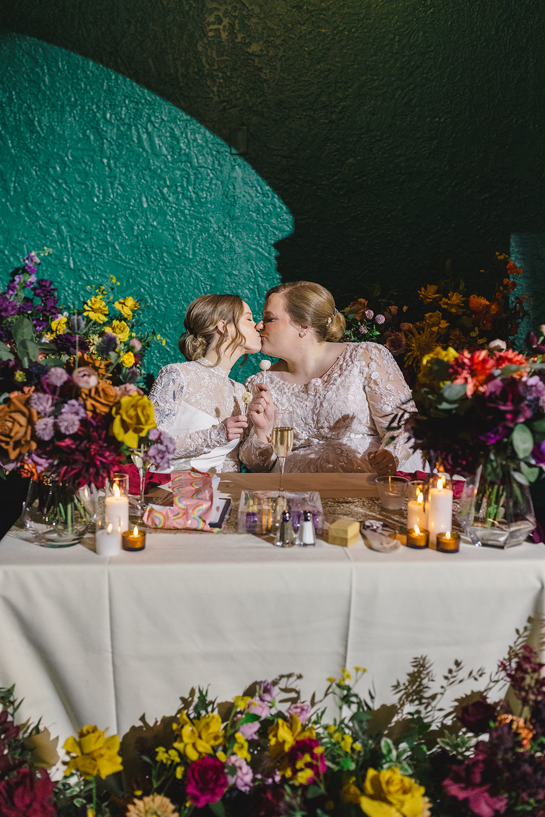 two brides kissing each other inside the uptown theater in kansas city they are at their wedding reception sitting at their table together 