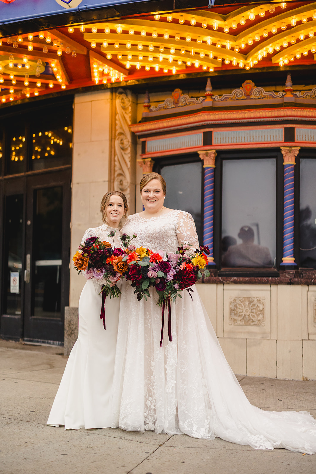 two brides taking wedding photos together in front of the uptown theater in kansas city 