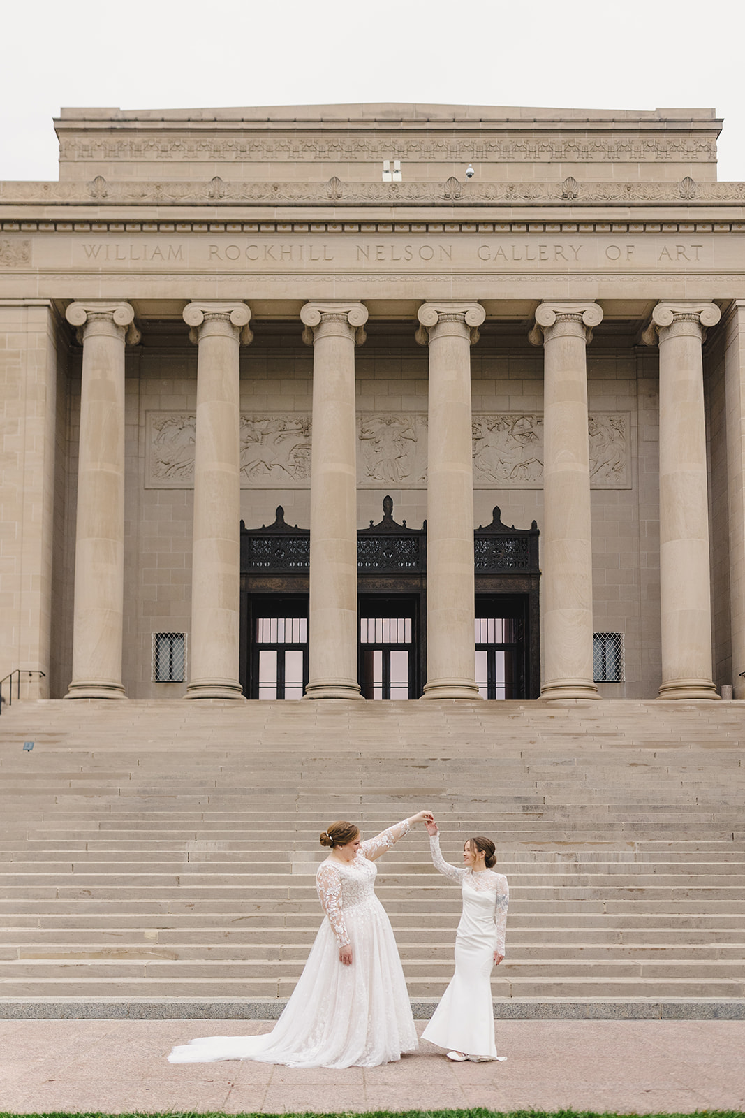 two brides in front of the nelson gallery of art in kansas city one bride is twirling the other 