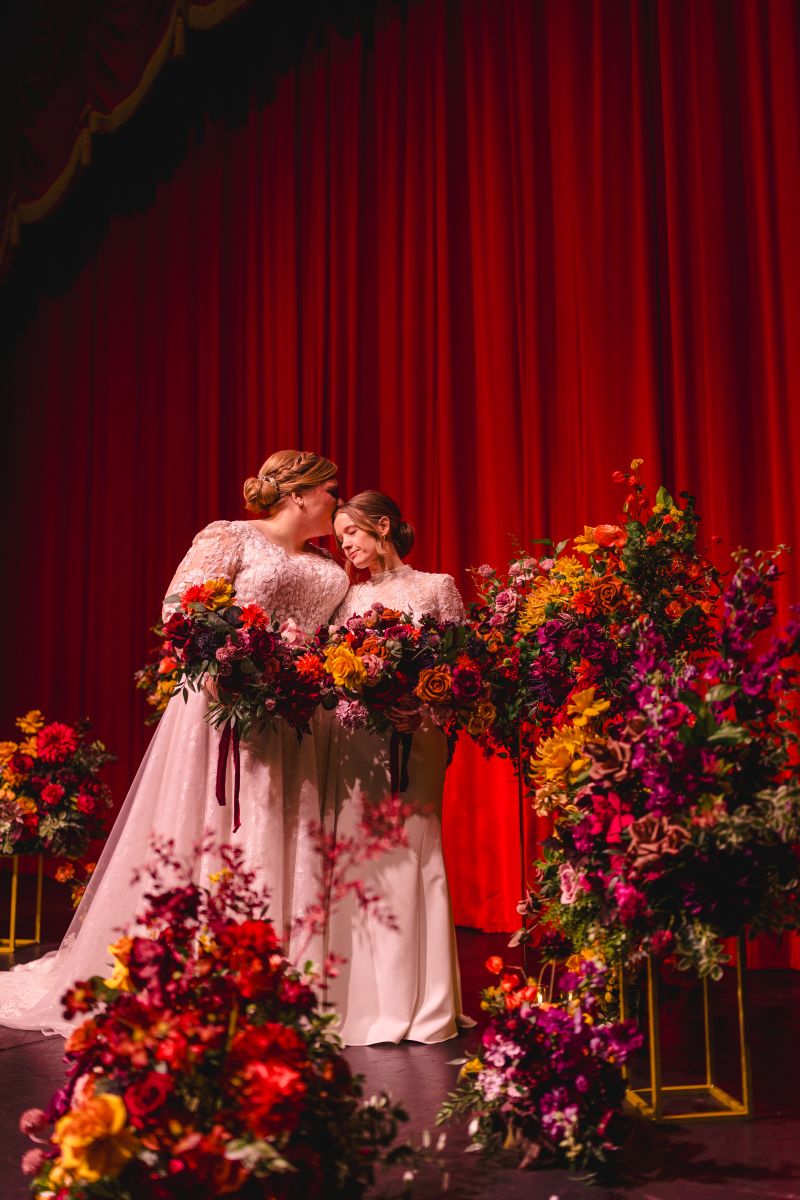 two brides taking wedding portraits together on the stage inside the uptown theater 