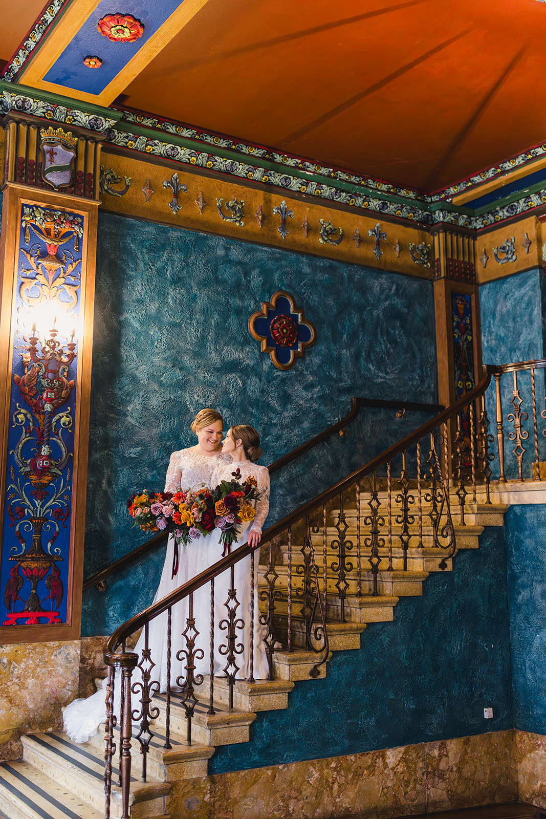 two brides on the day of their wedding standing on the staircase inside uptown theater in kansas city 