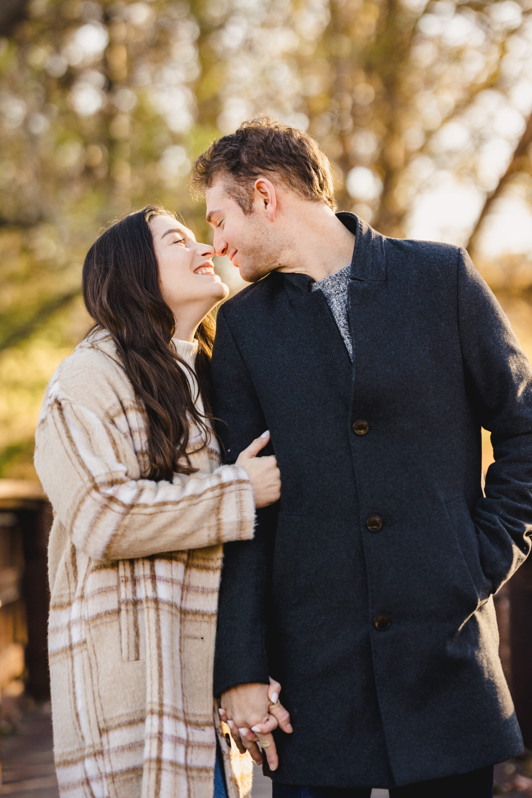 a woman wearing a plaid coat hugging her partner's arm and smiling up at him during their fall engagement session 
