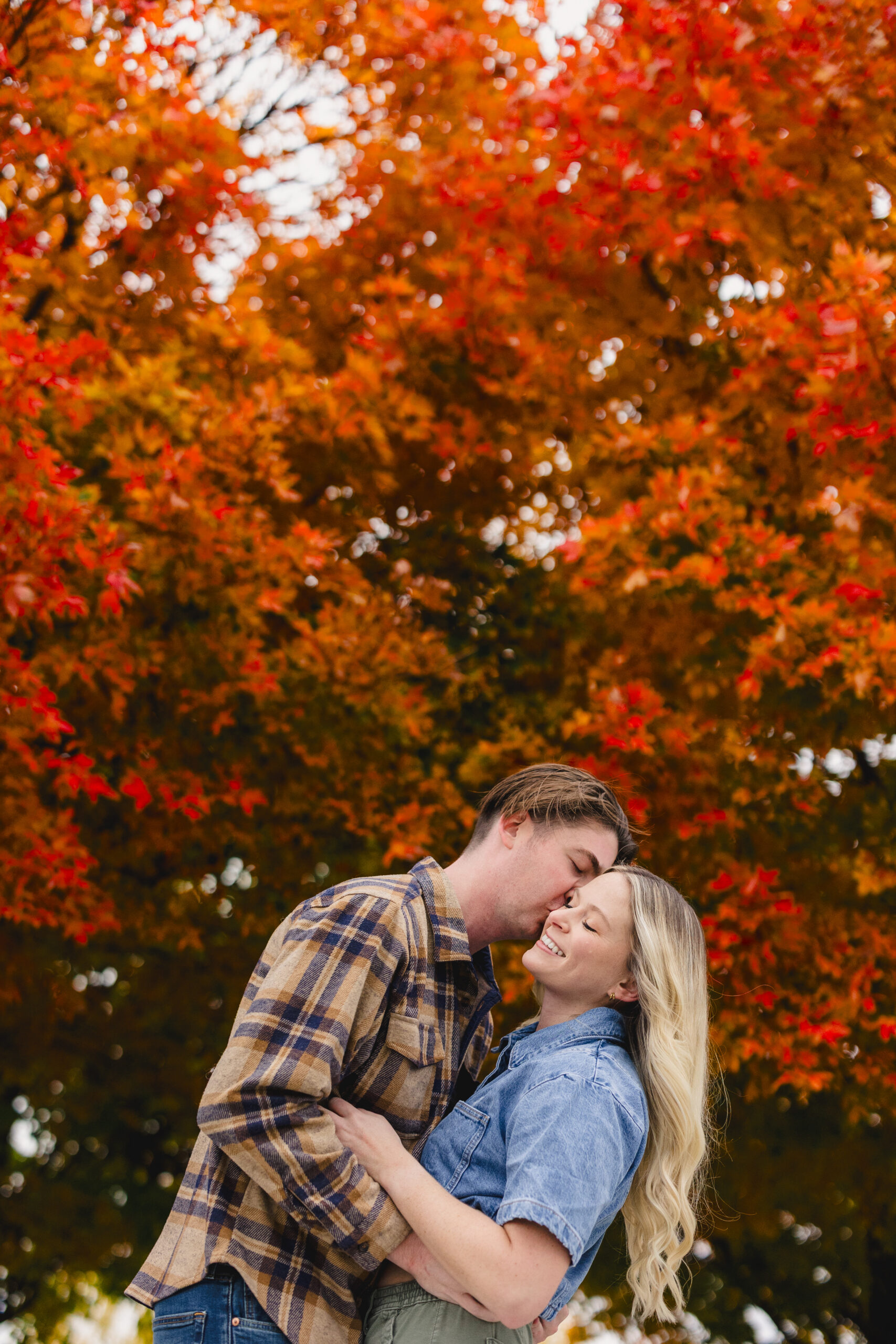 a man kissing his partner on the cheek during their fall engagement session