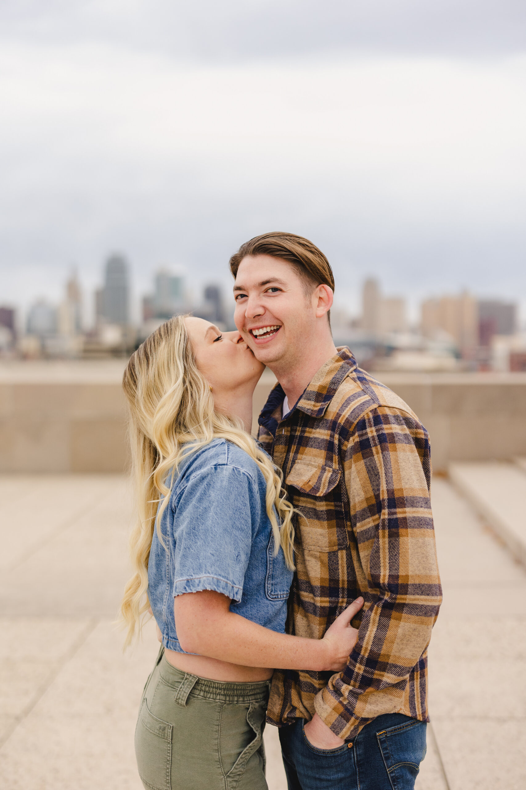 a woman embracing her partner and kissing him on the cheek with the kansas city skyline behind them 